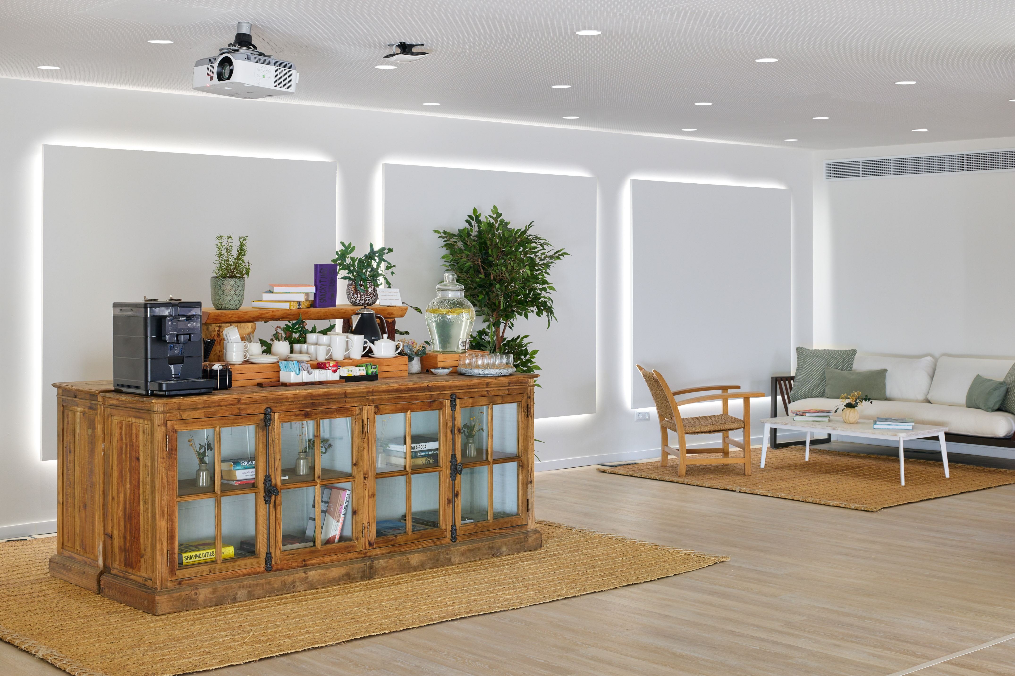 Modern lounge with coffee station, wooden credenza, sofa, and projector.