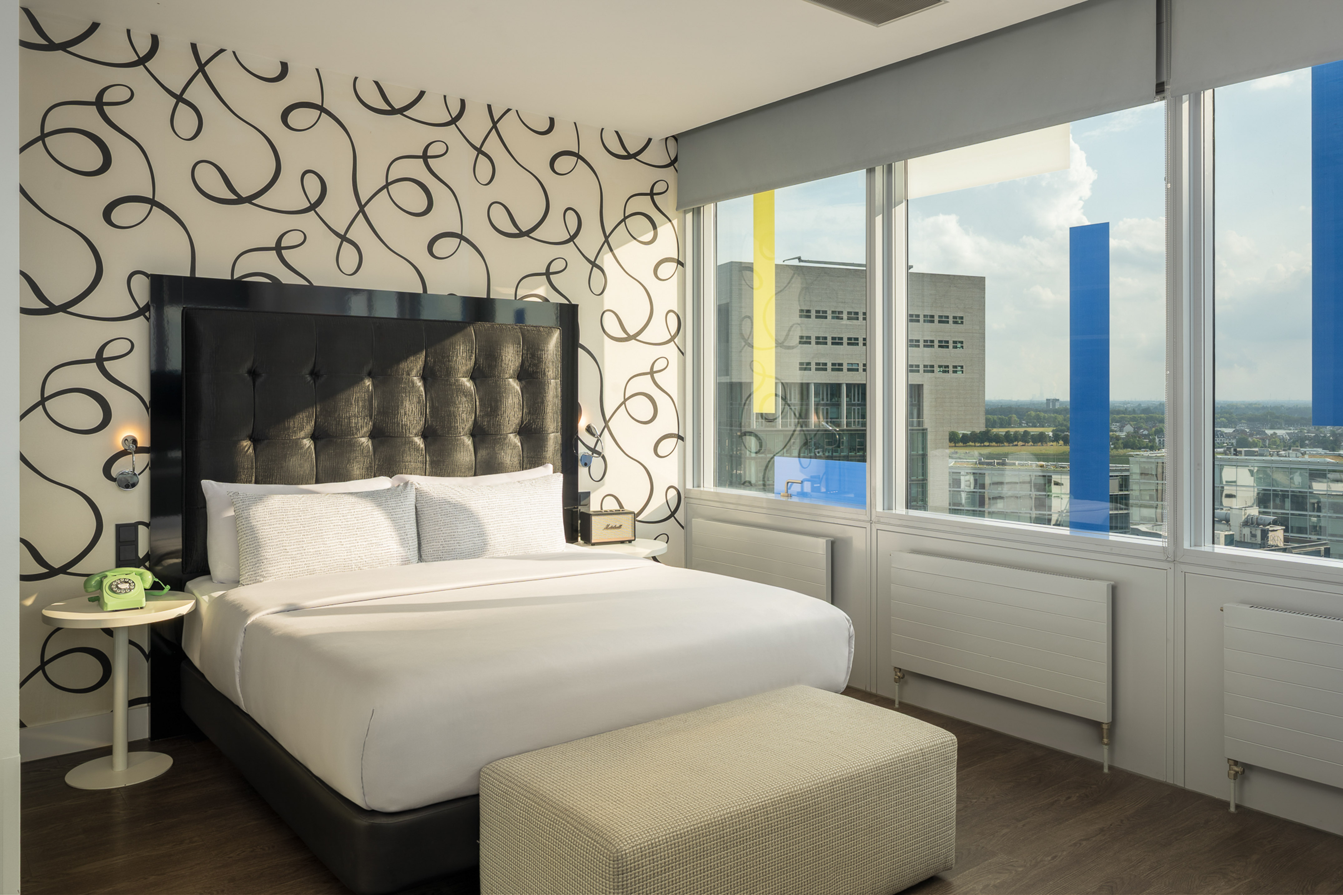 Hotel bedroom with king bed, black headboard, unique swirling wallpaper, city view.