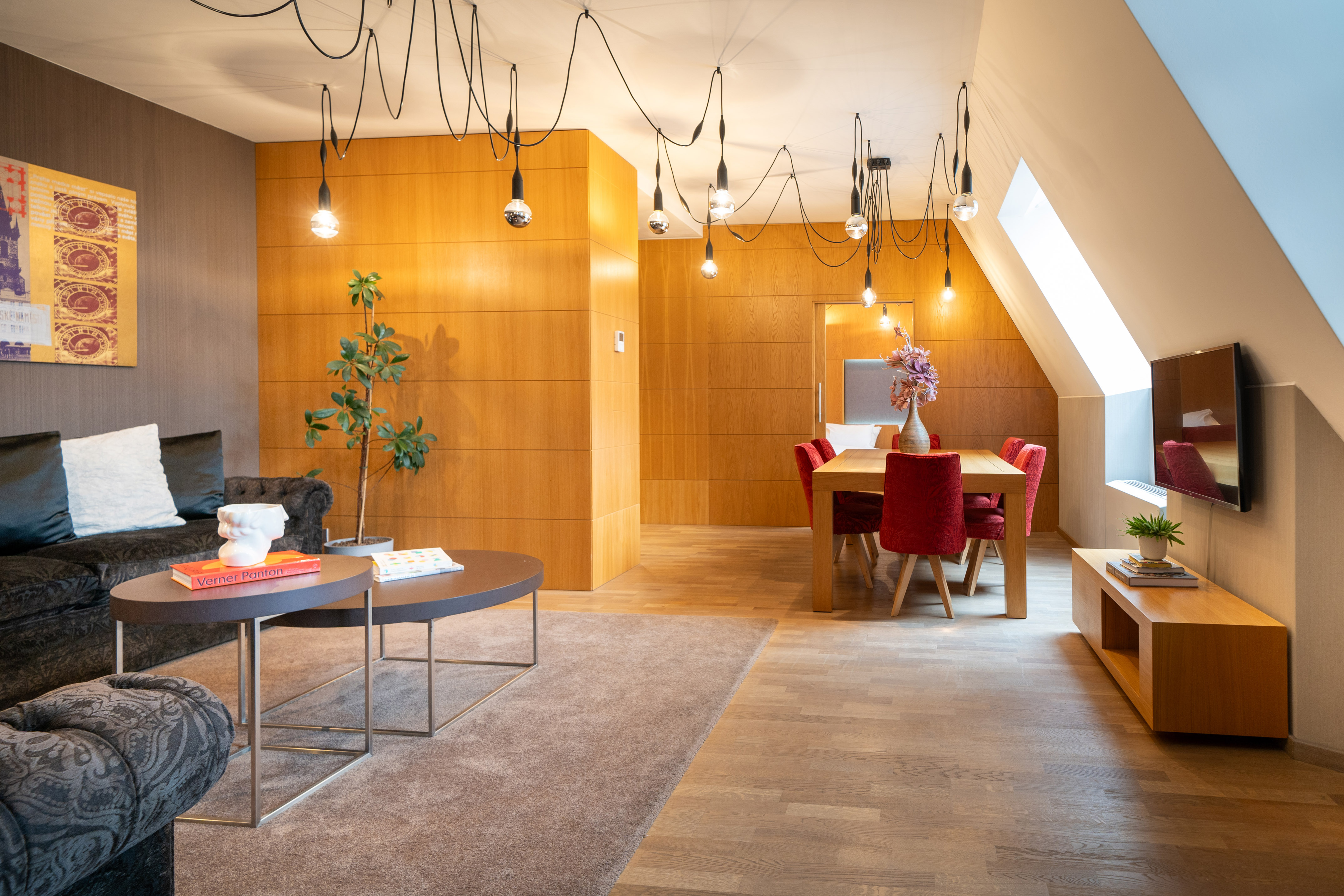 Modern apartment living dining, wood walls, industrial lighting, red chairs.