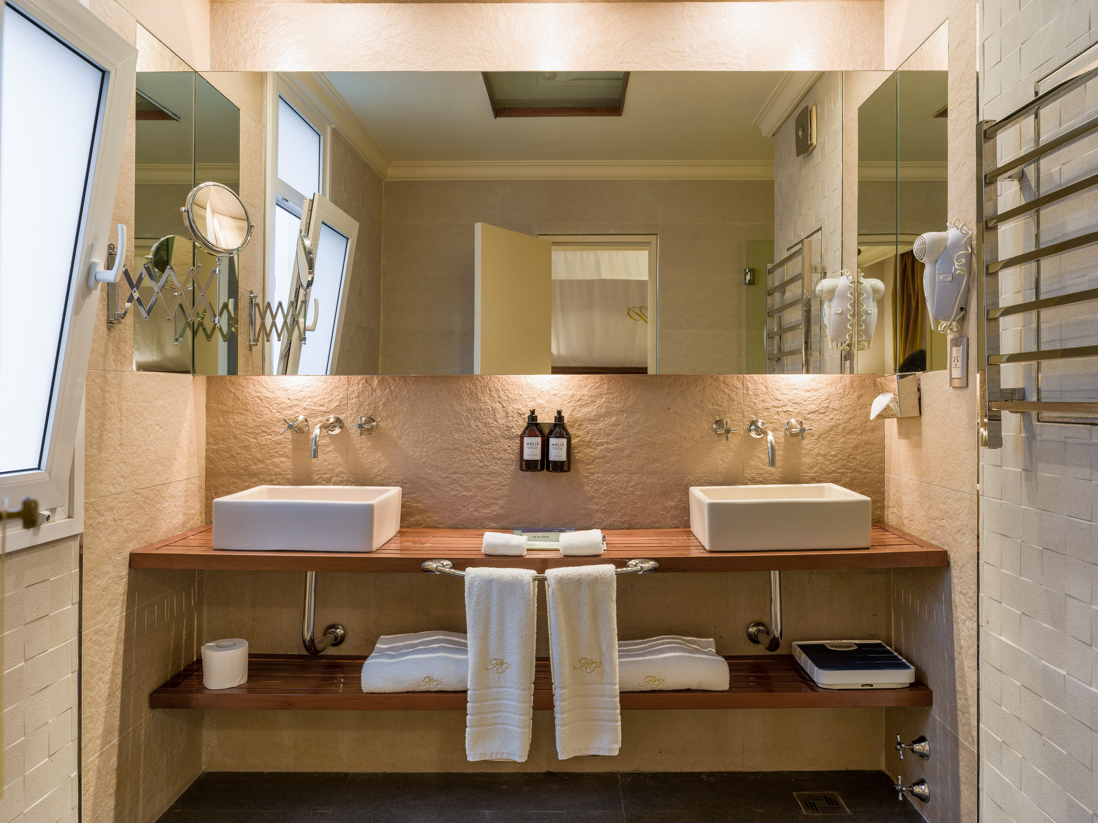 Modern bathroom with double sinks, wooden vanity, large mirror, and white towels.