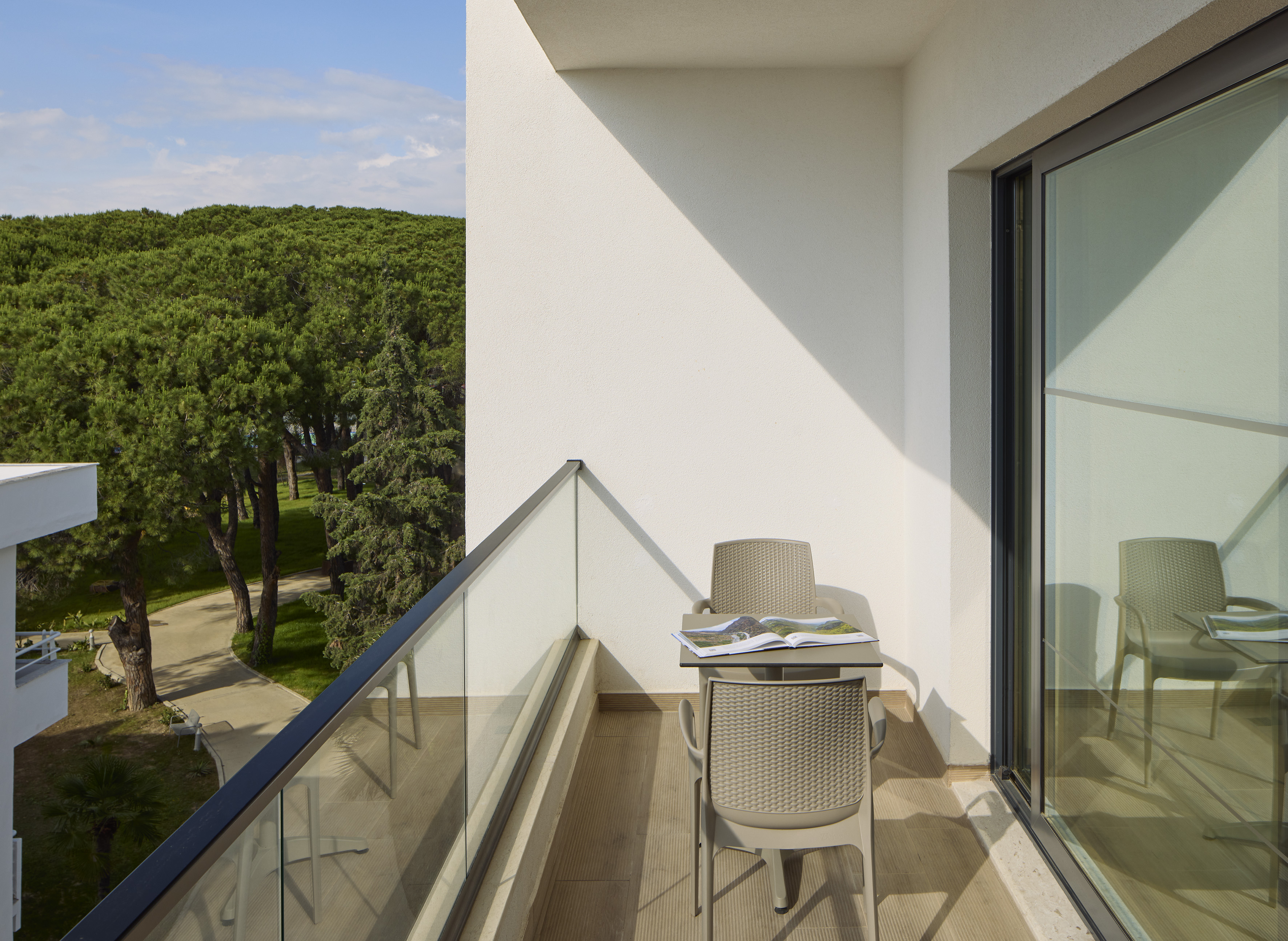 Modern balcony with outdoor seating, glass railing, and lush green forest view.