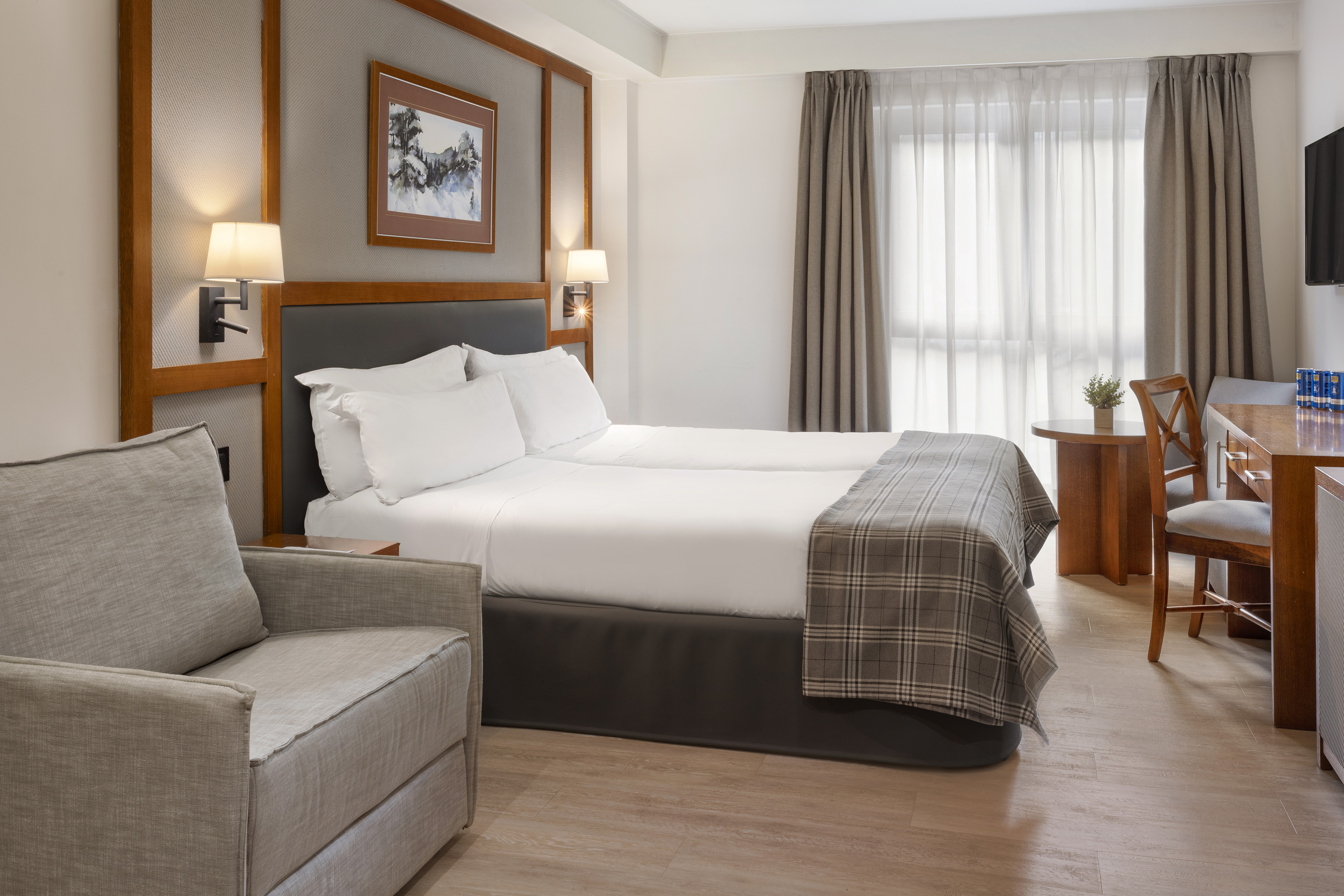 Comfortable hotel room with twin beds, armchair, and wooden desk.