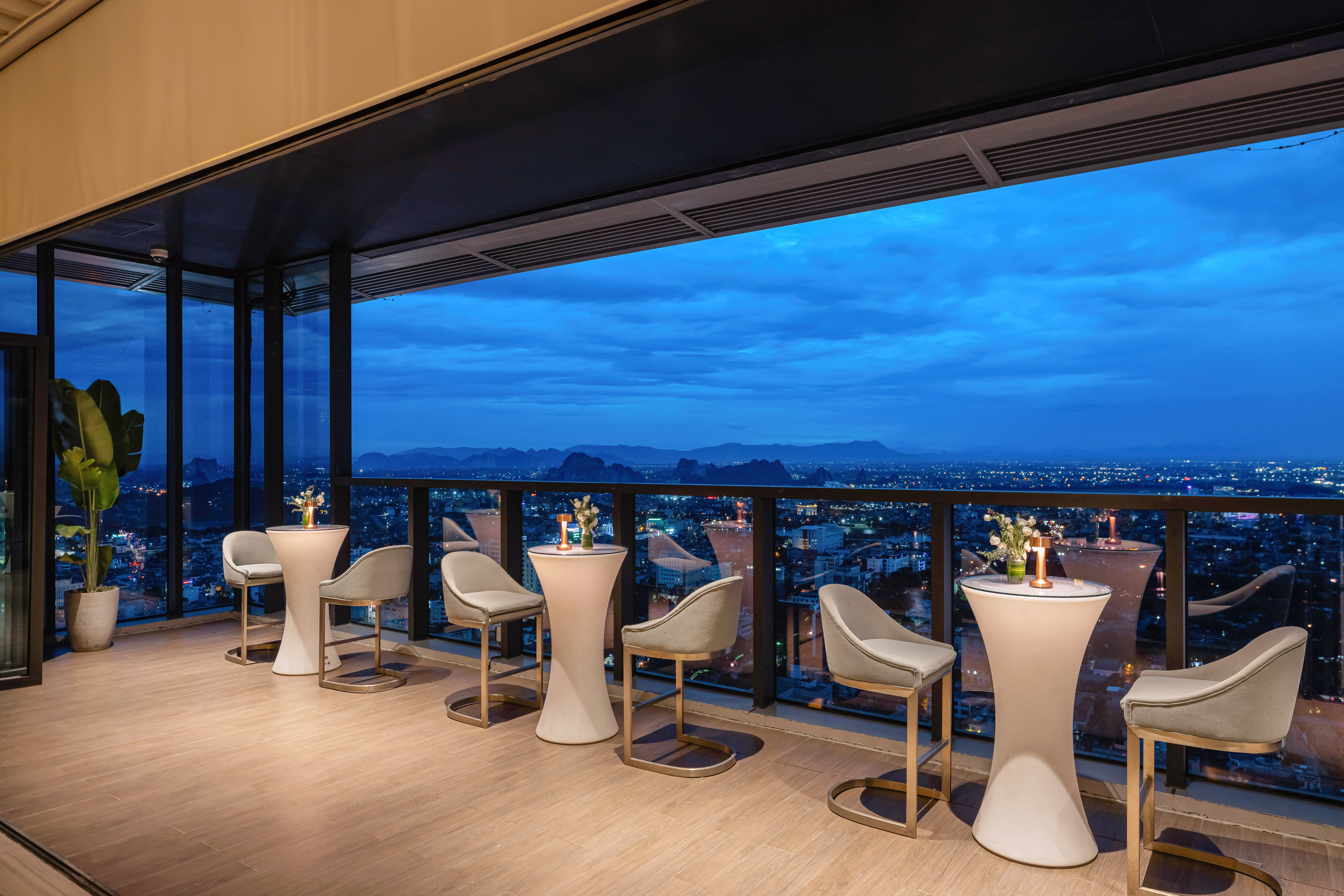 Rooftop bar terrace at dusk with city skyline view and modern seating.
