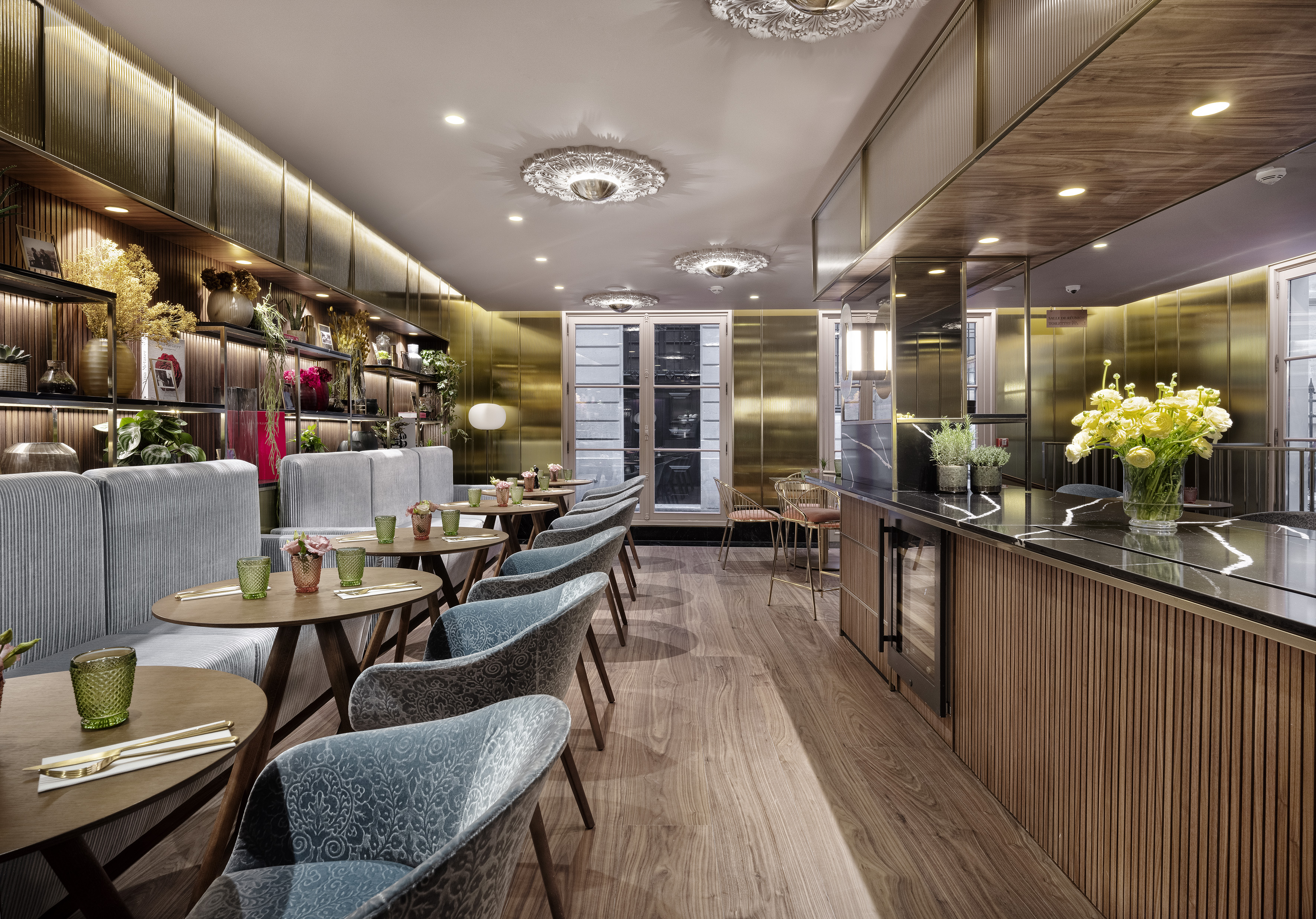Restaurant dining area with blue chairs, wooden tables, gold walls, and a bar.