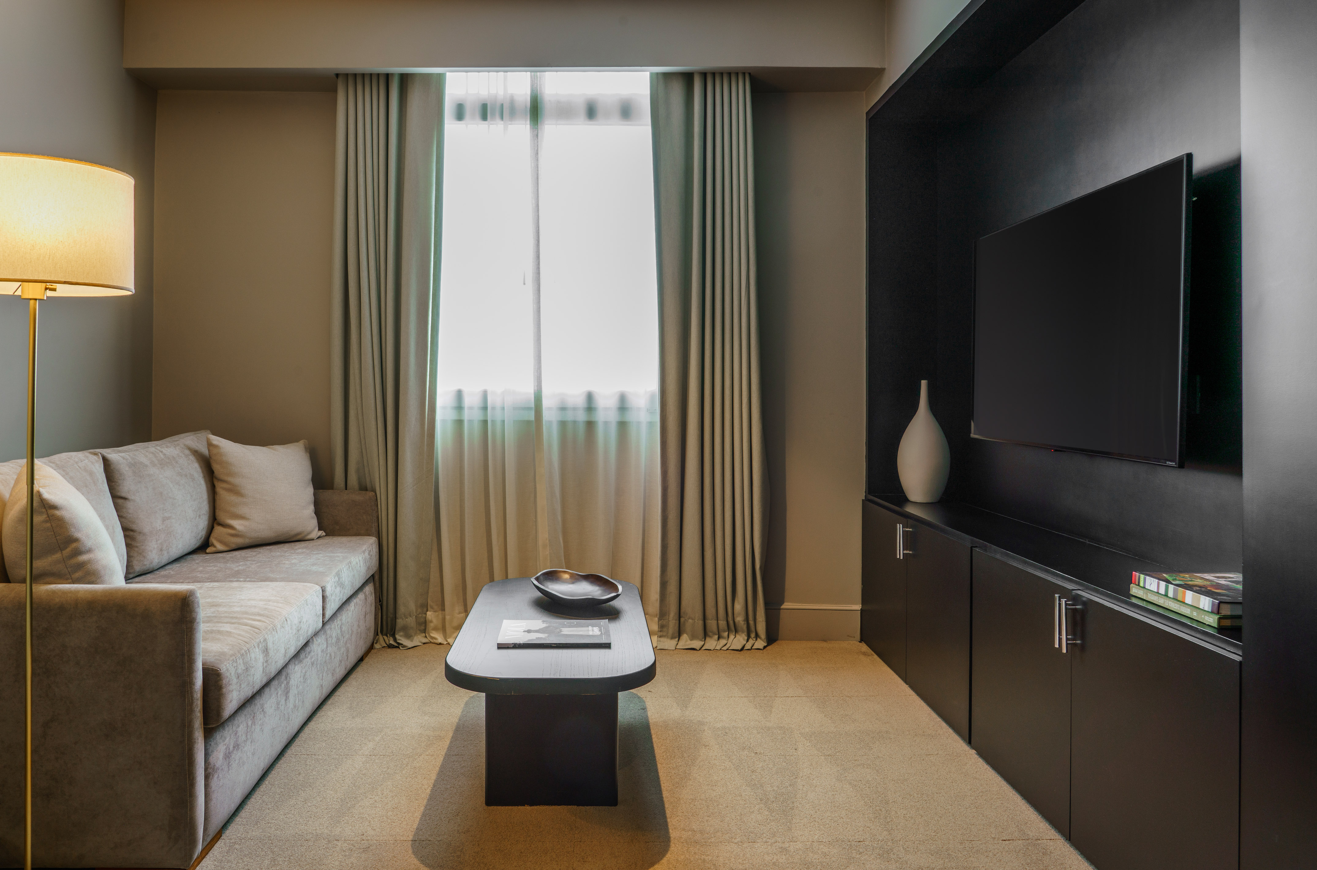 Modern hotel suite living room with sofa, coffee table, and TV console.