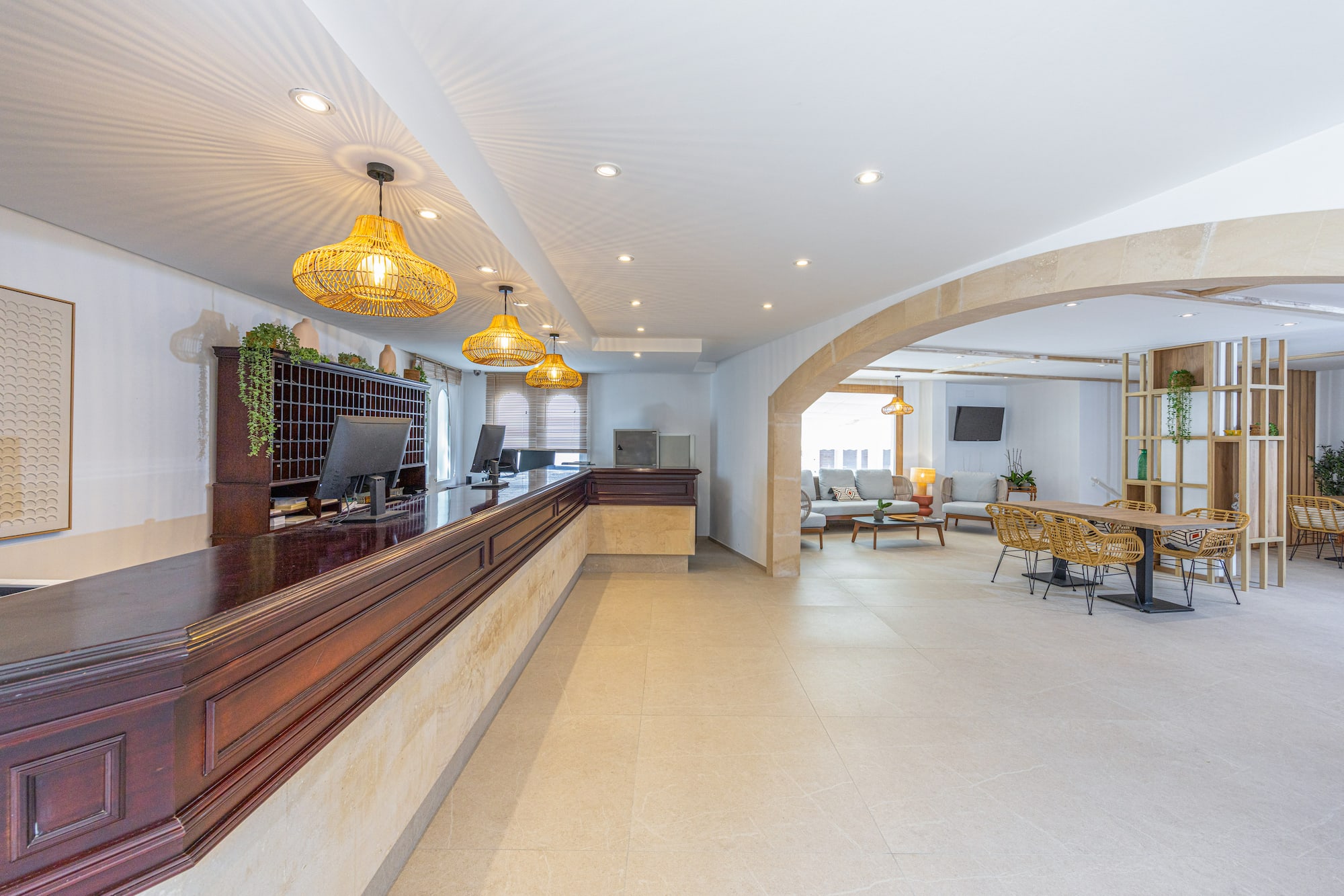 Hotel reception lobby with dark wood desk, rattan lights, and lounge area.