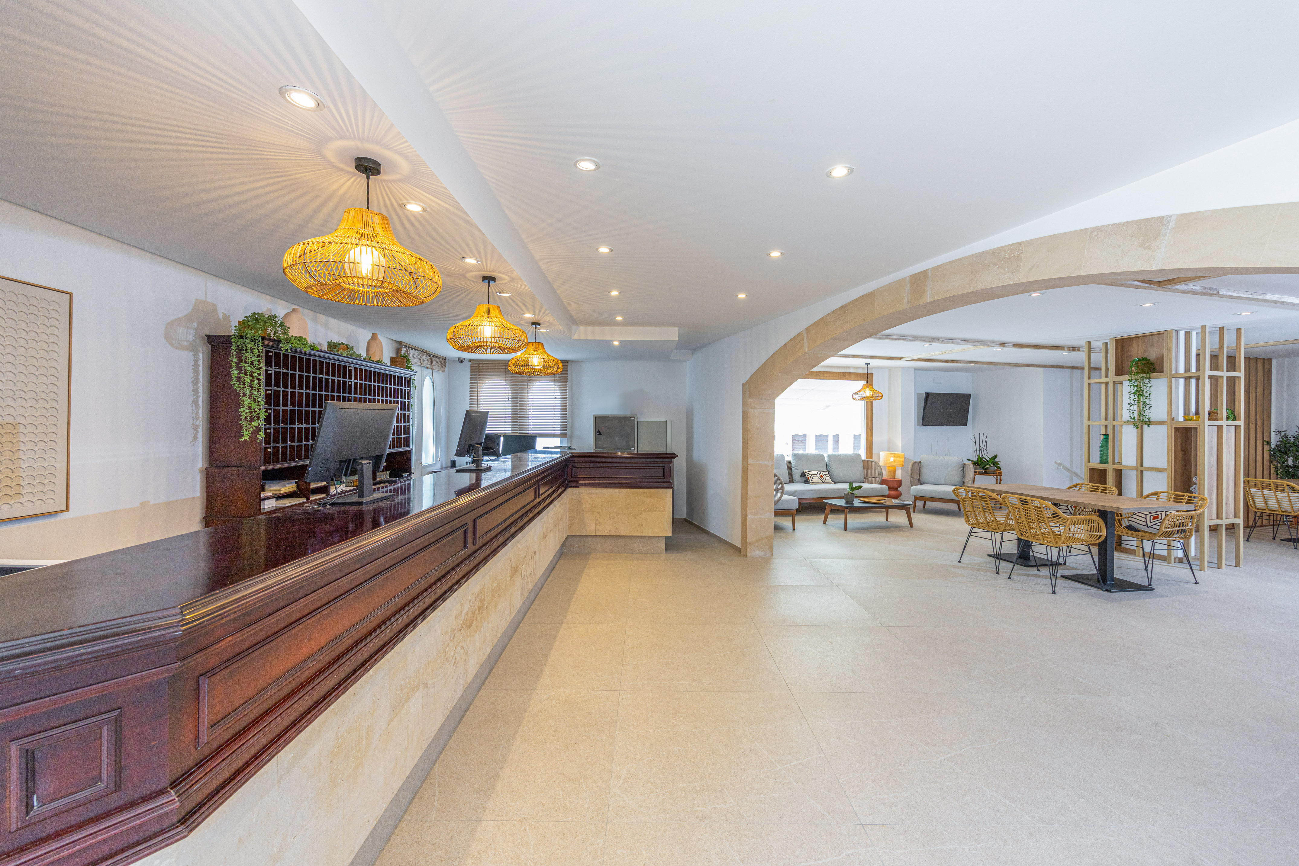 Hotel reception lobby with dark wood desk, rattan lights, and lounge area.