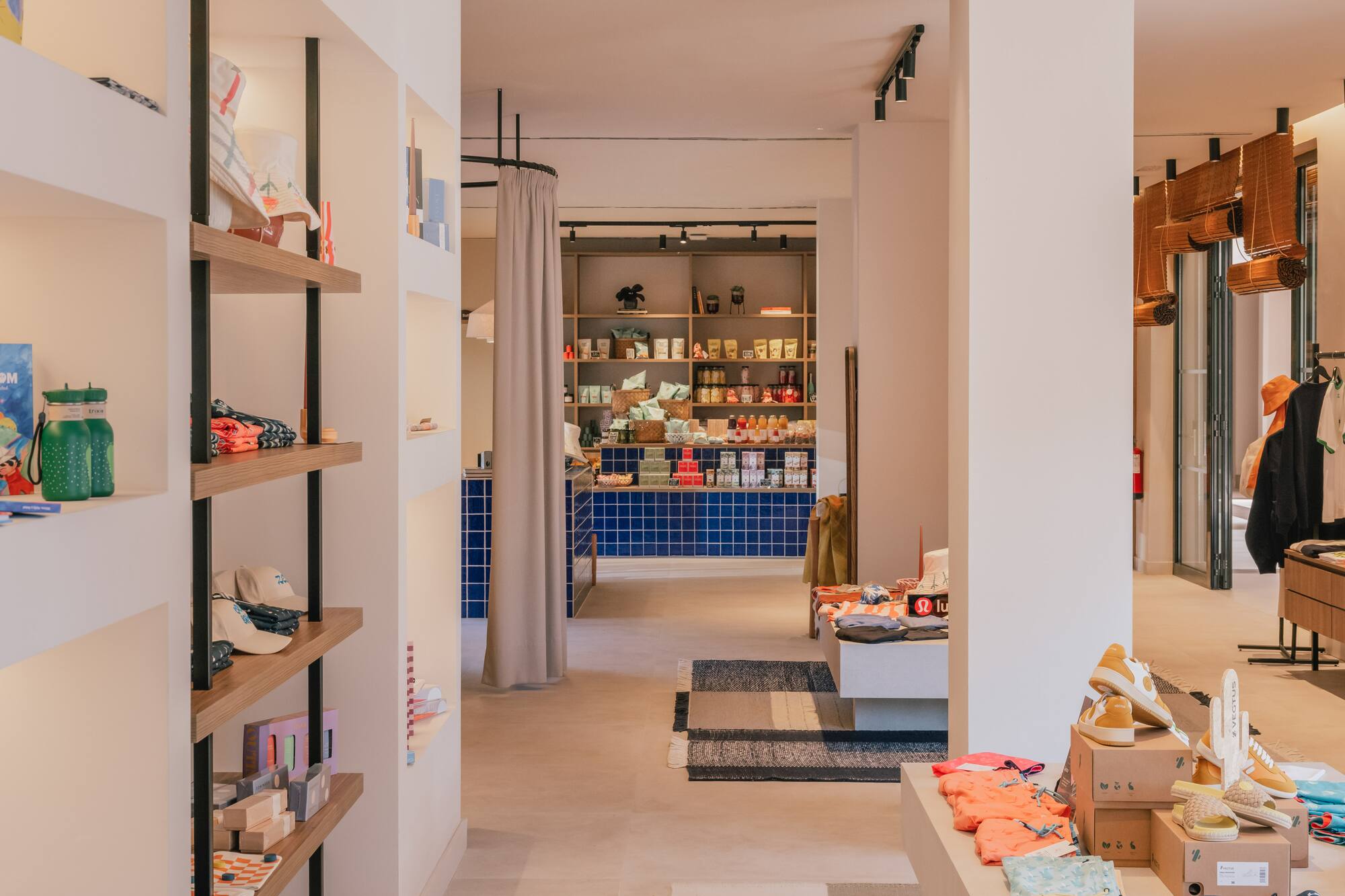 Modern boutique interior with shelves of retail products, clothing displays, and blue tiled counter.