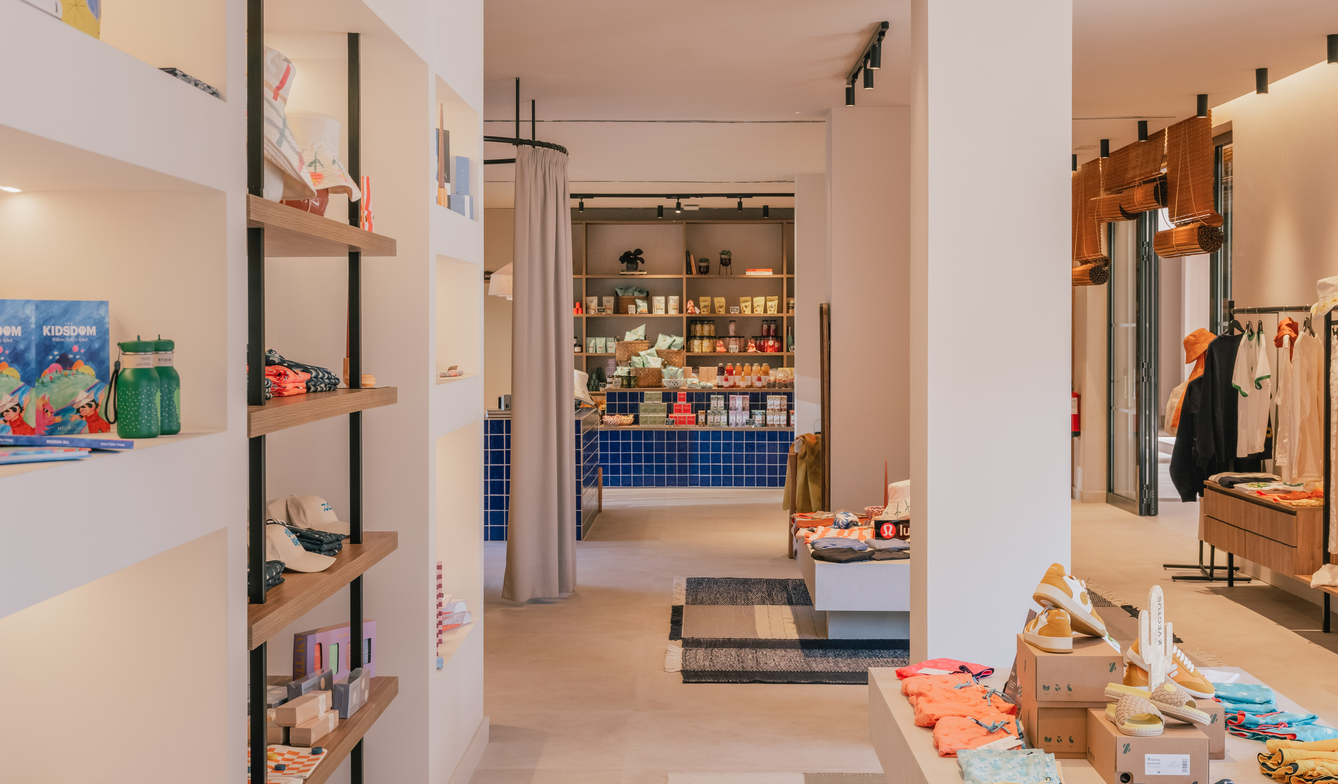 Modern boutique interior with shelves of retail products, clothing displays, and blue tiled counter.