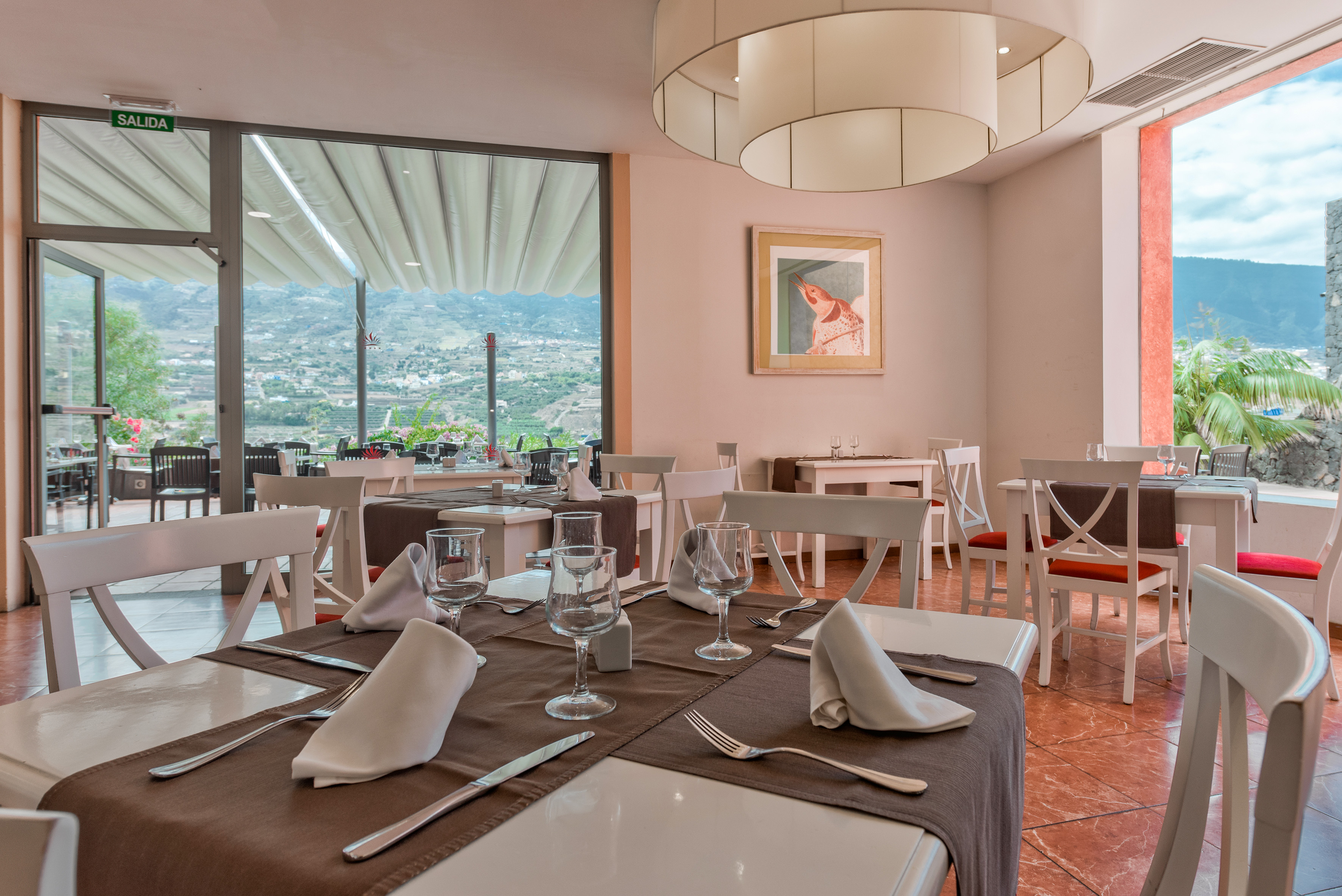 Restaurant dining room with set tables, white chairs, and scenic mountain valley views.