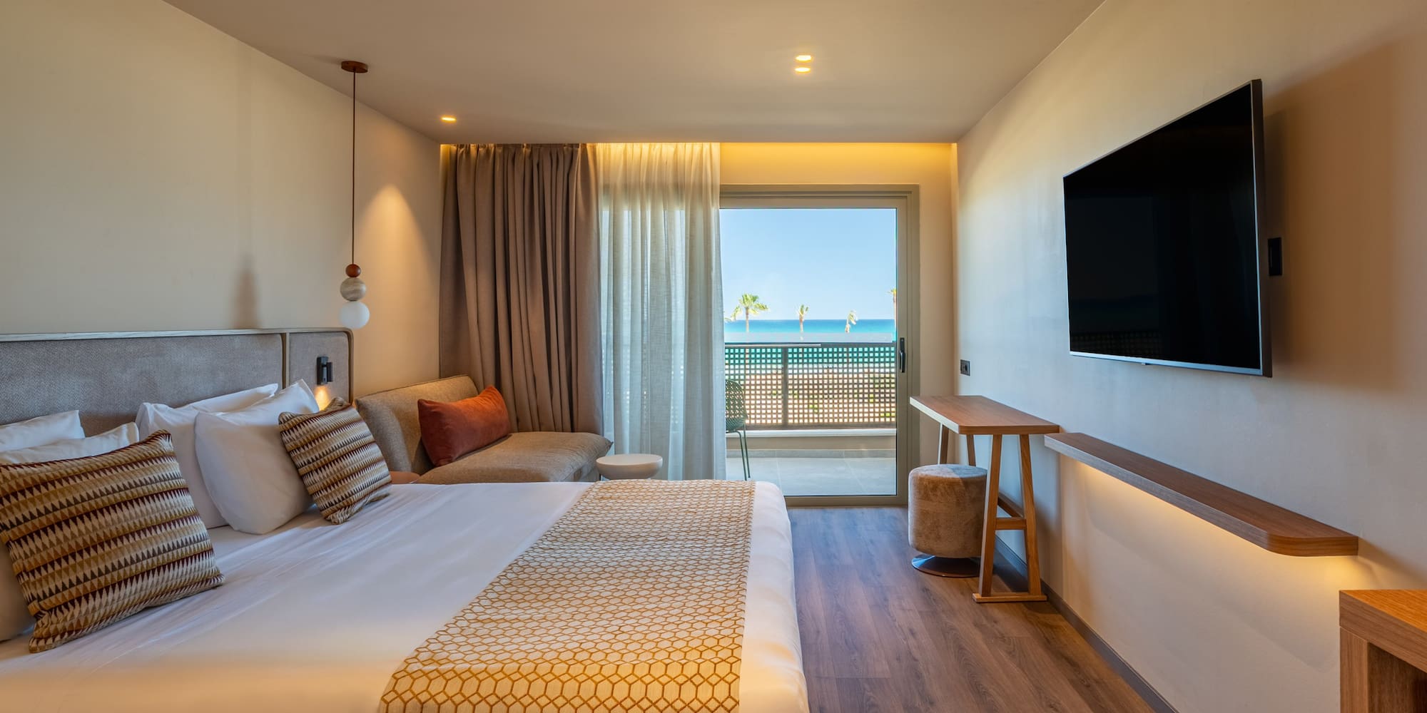 Beachfront hotel room with modern bed, sea view balcony, and flat-screen TV.