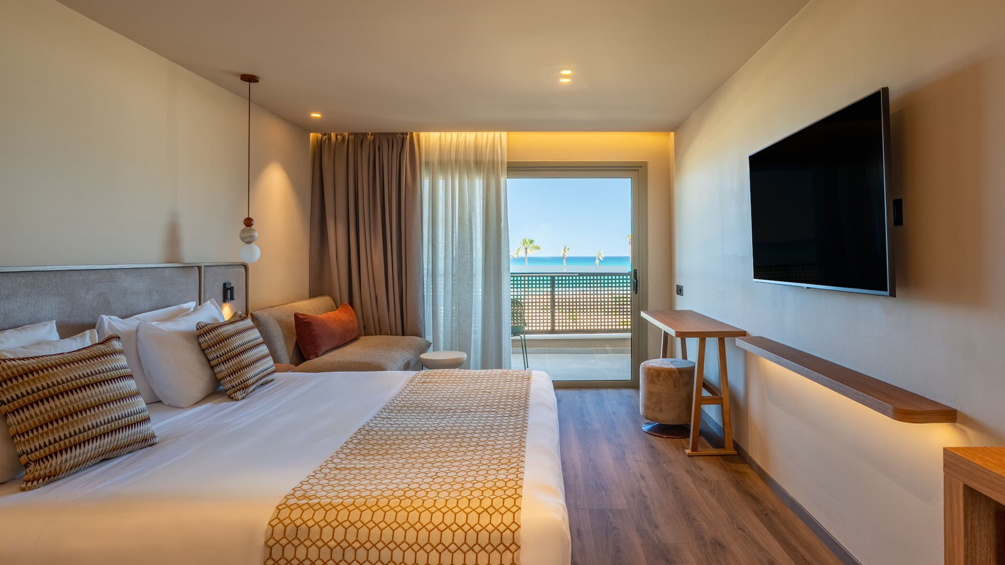 Beachfront hotel room with modern bed, sea view balcony, and flat-screen TV.