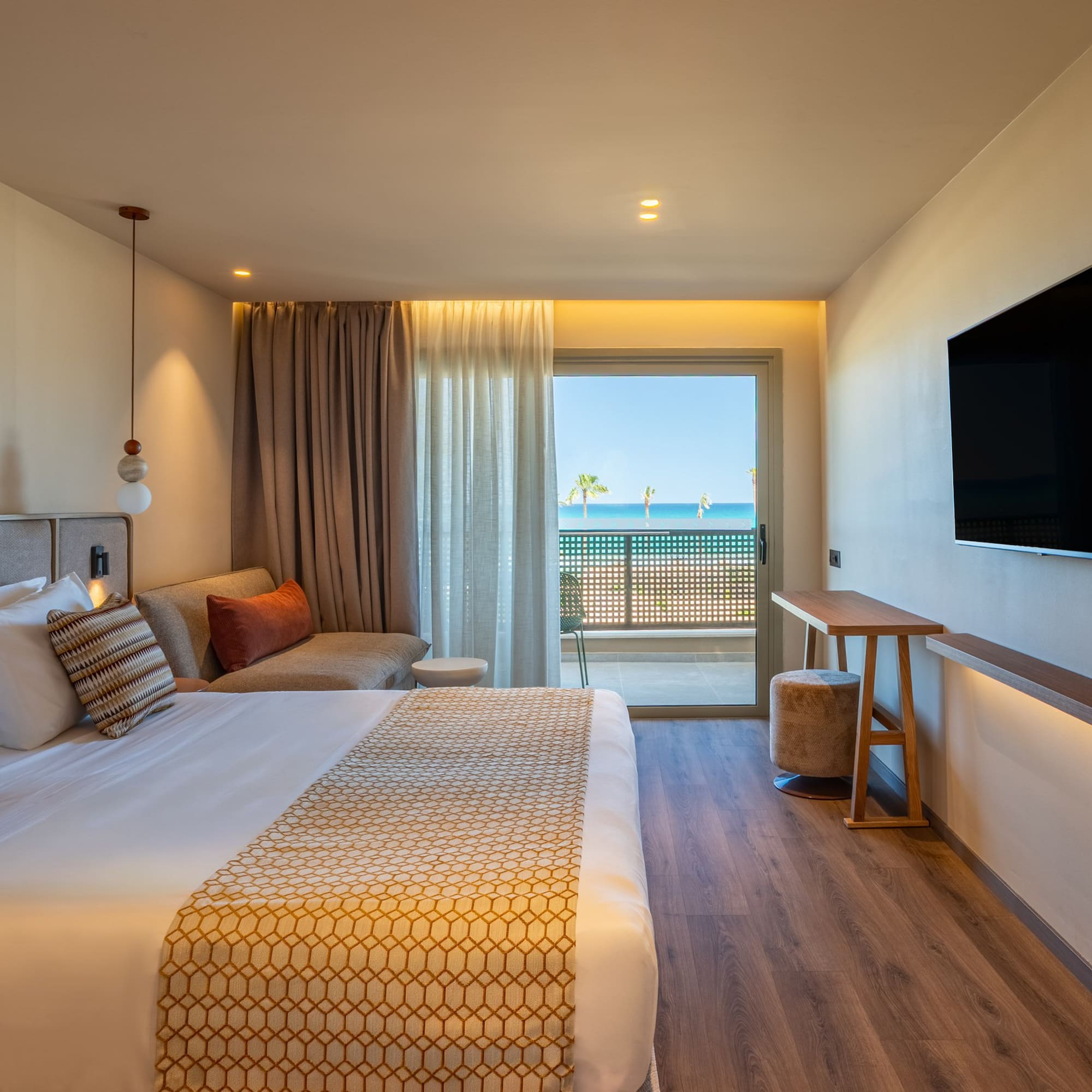 Beachfront hotel room with modern bed, sea view balcony, and flat-screen TV.