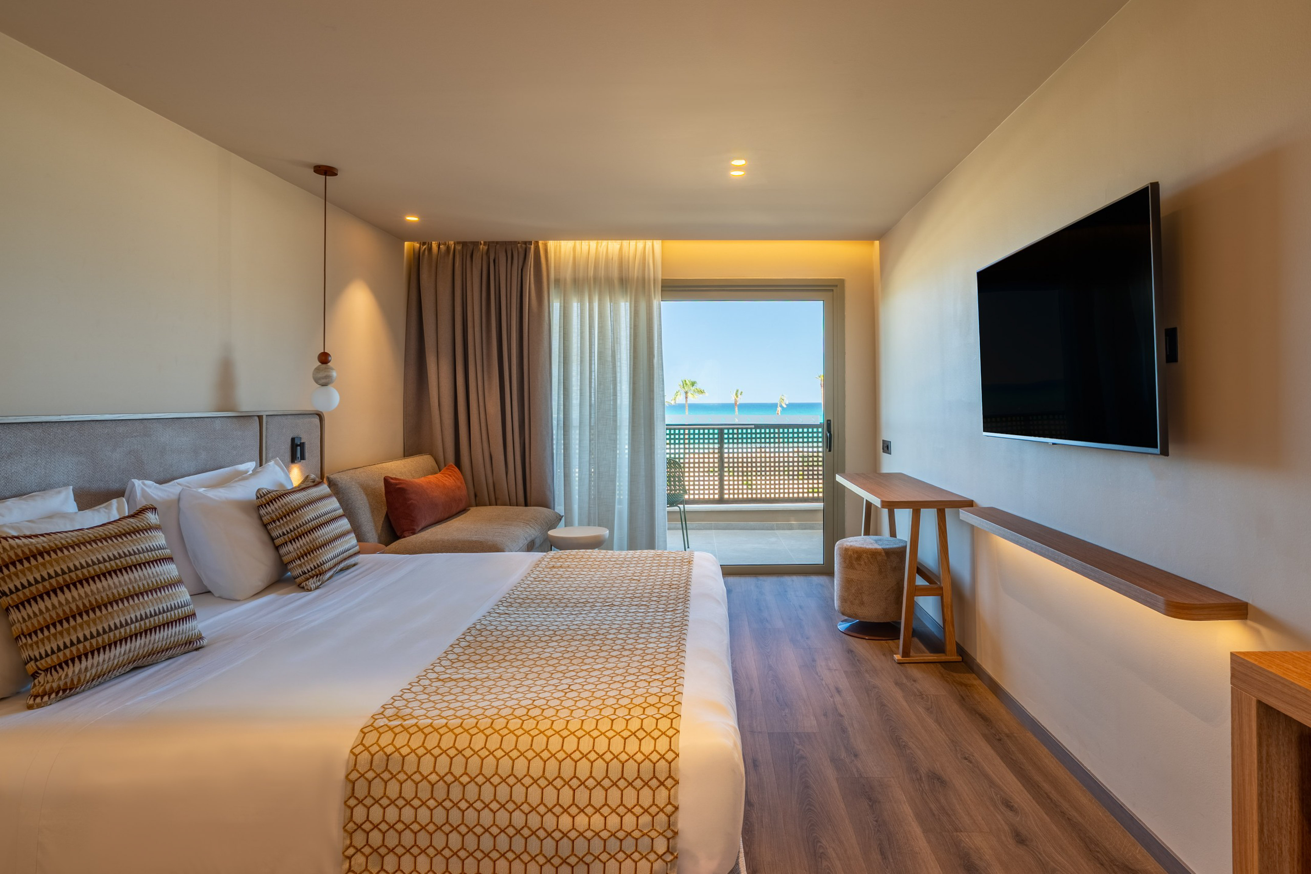 Beachfront hotel room with modern bed, sea view balcony, and flat-screen TV.
