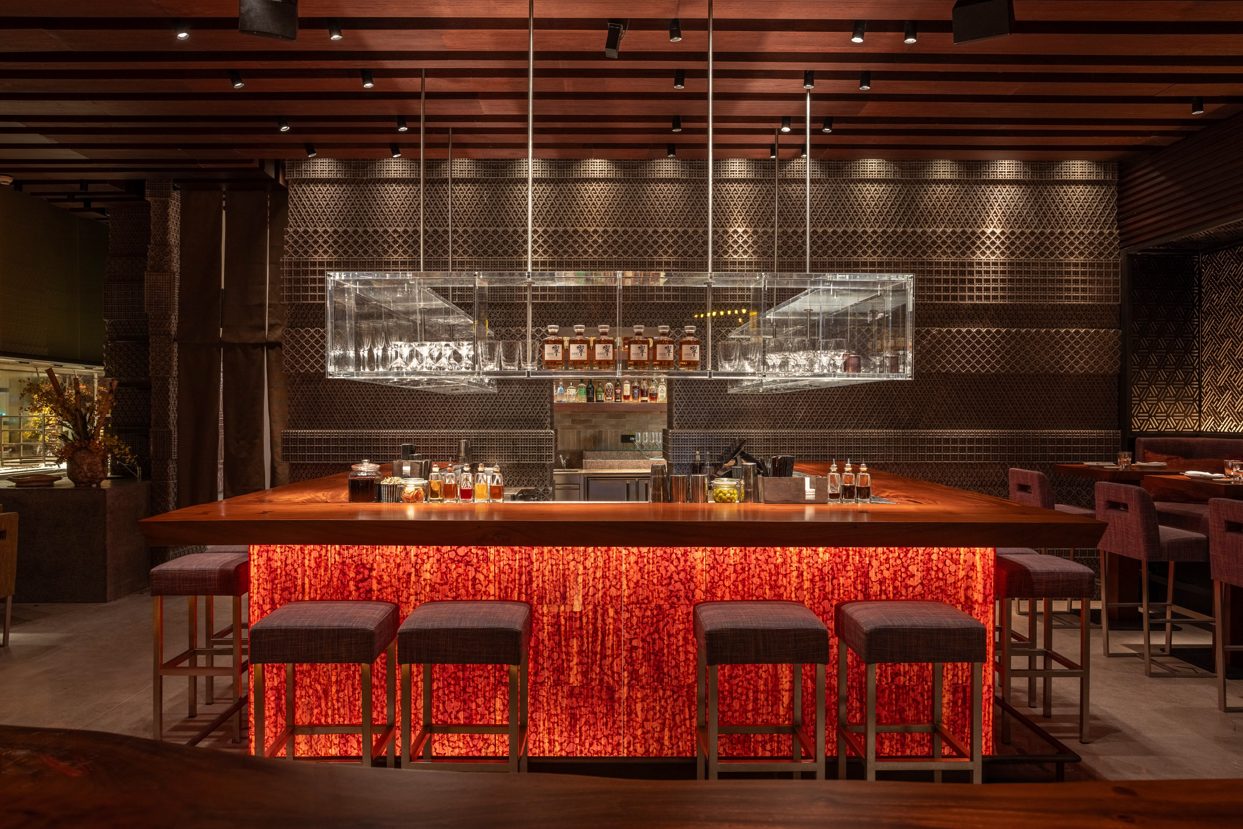 Modern restaurant bar with illuminated red counter, wooden top, and stylish stools.