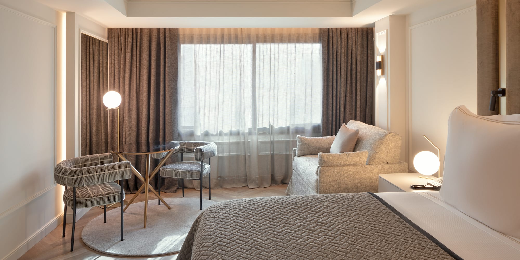 Habitación de hotel moderna: cama, zona de estar, mesa, sillas y ventanal.