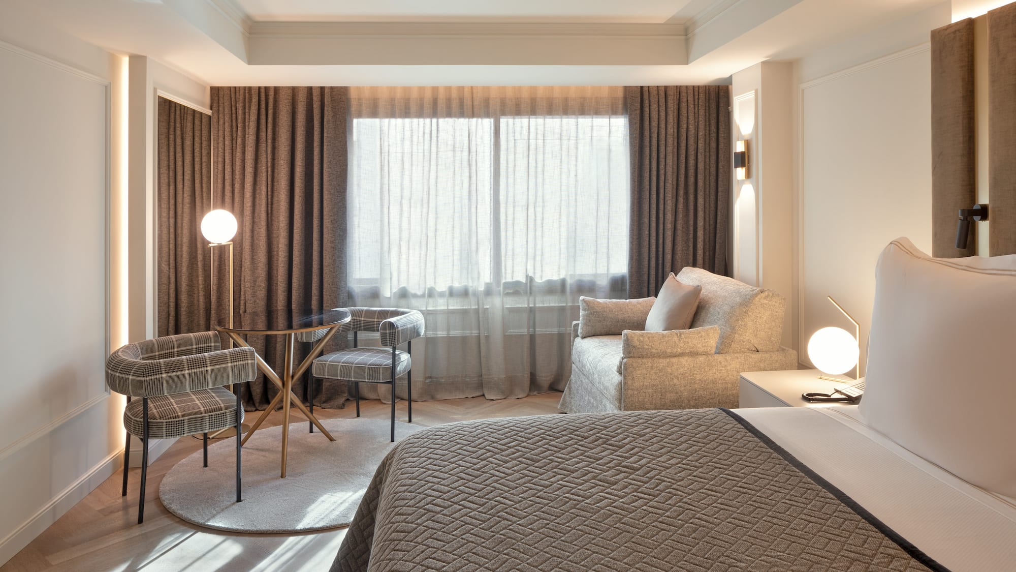 Habitación de hotel moderna: cama, zona de estar, mesa, sillas y ventanal.
