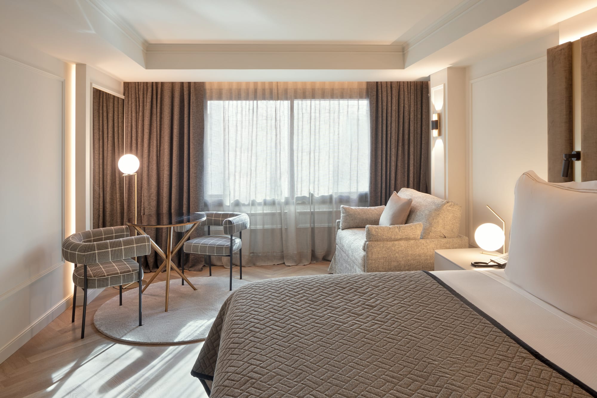 Habitación de hotel moderna: cama, zona de estar, mesa, sillas y ventanal.
