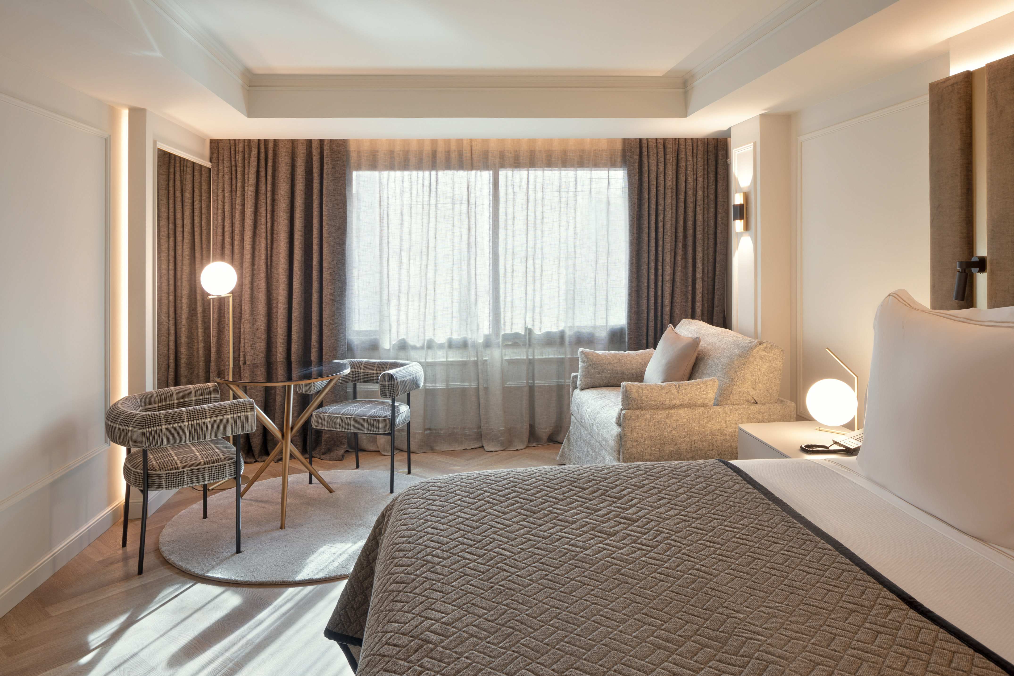 Habitación de hotel moderna: cama, zona de estar, mesa, sillas y ventanal.