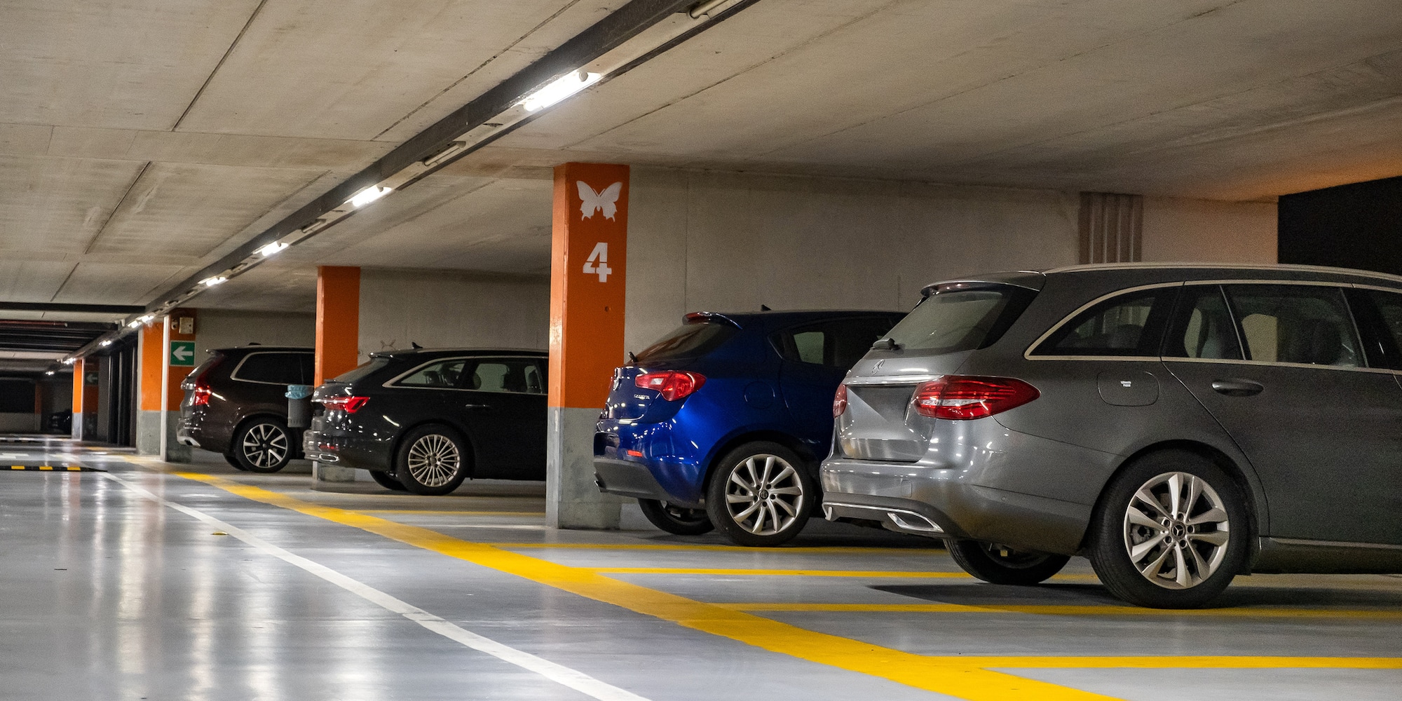 Modern underground parking garage with parked cars and fluorescent lights.