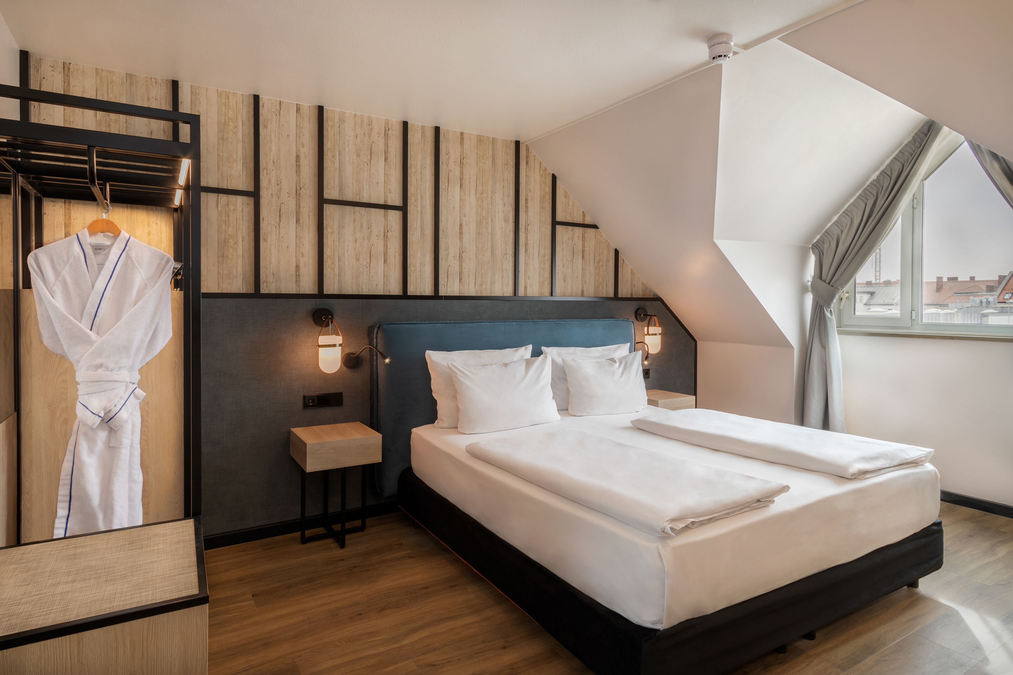 Modern hotel room with double bed, wood paneling, bathrobe, and lamps.