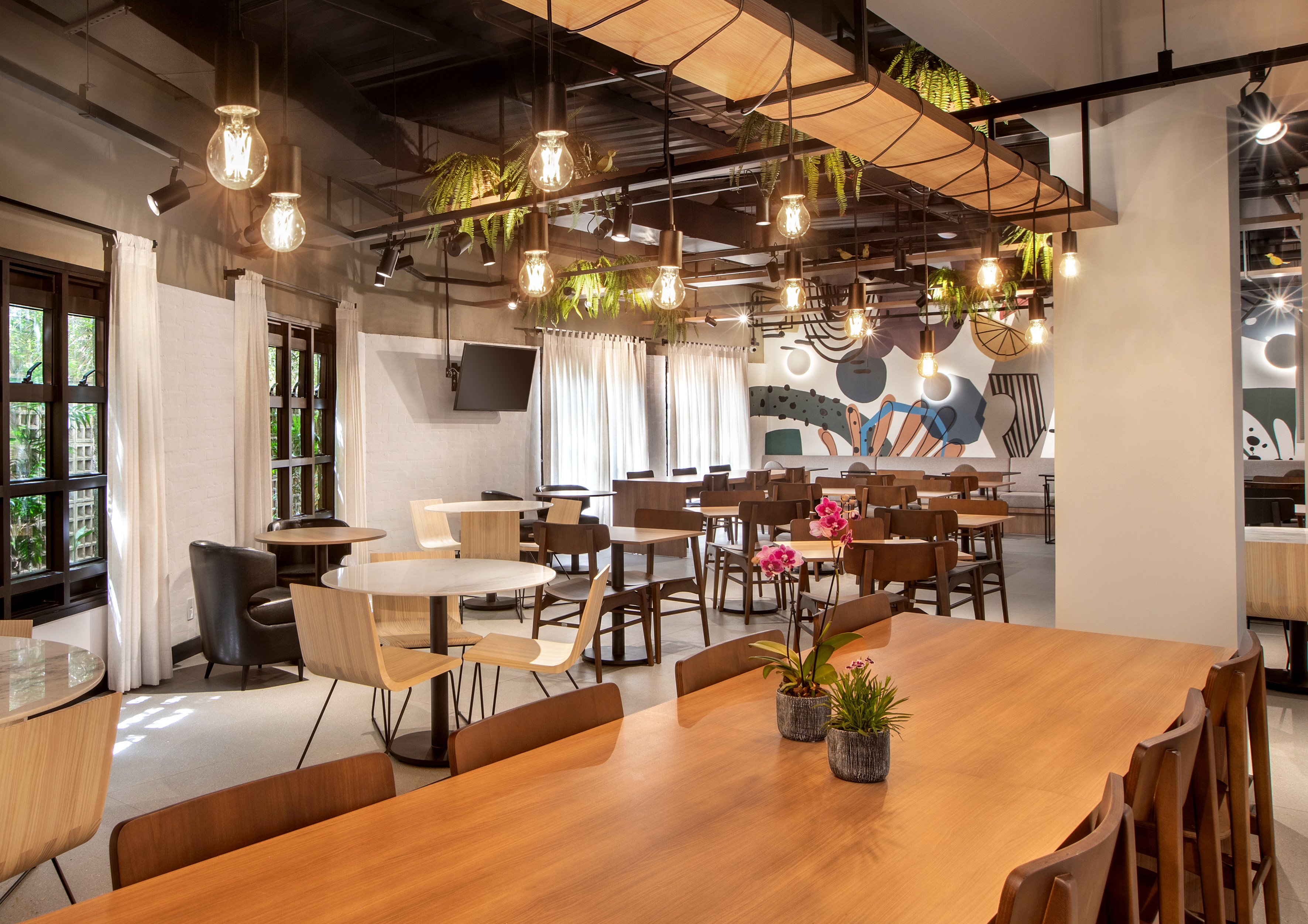 Contemporary cafe interior with wooden tables, plants, and abstract mural.
