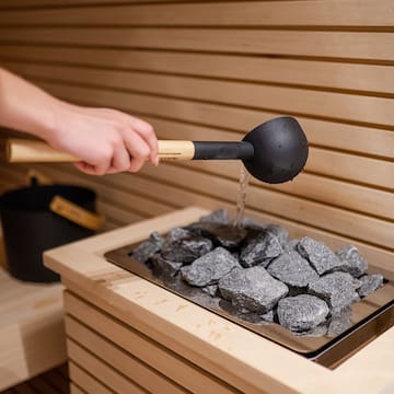 a person pouring water into a hot sauna
