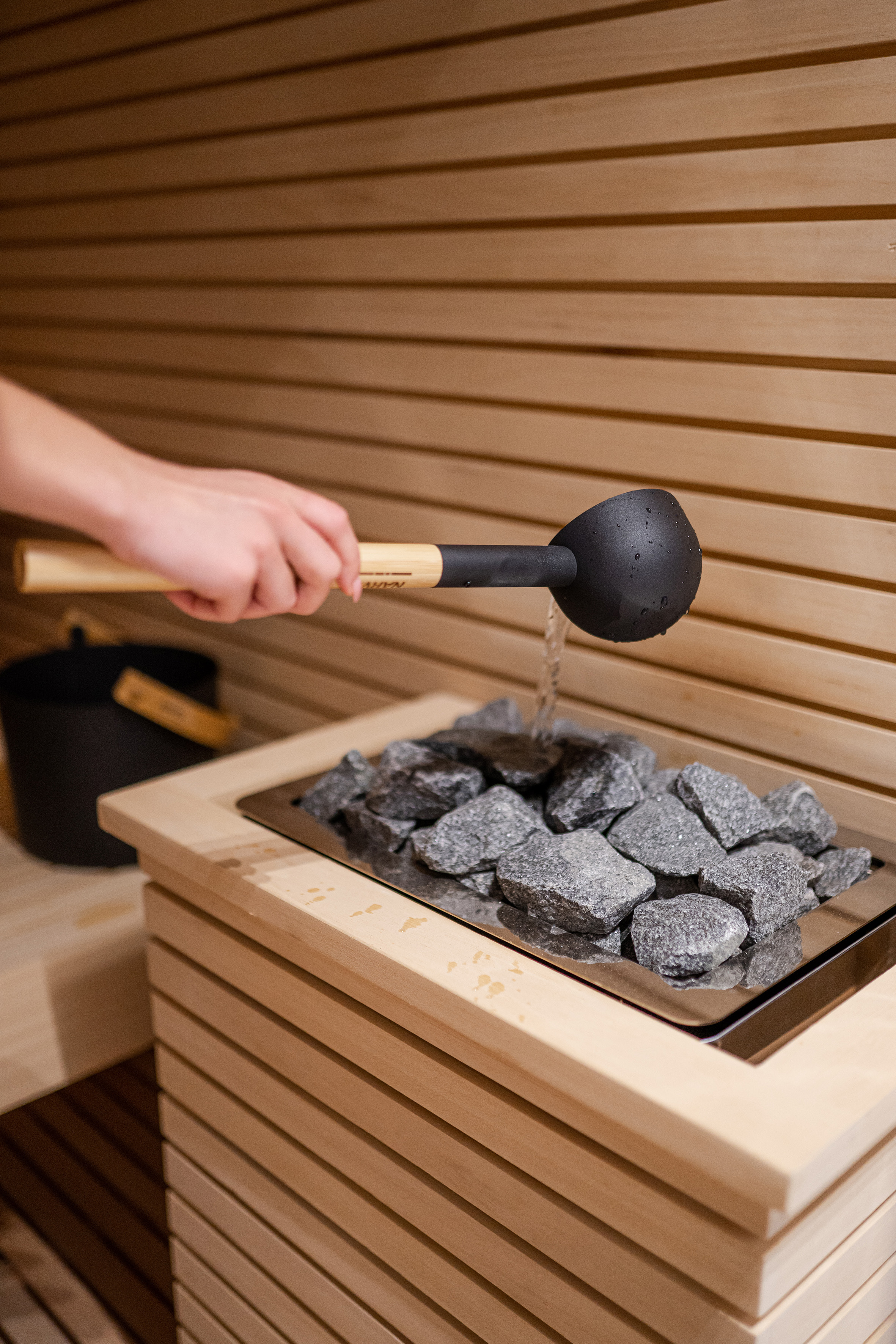 Pouring water onto hot sauna rocks from a ladle in a wooden sauna.