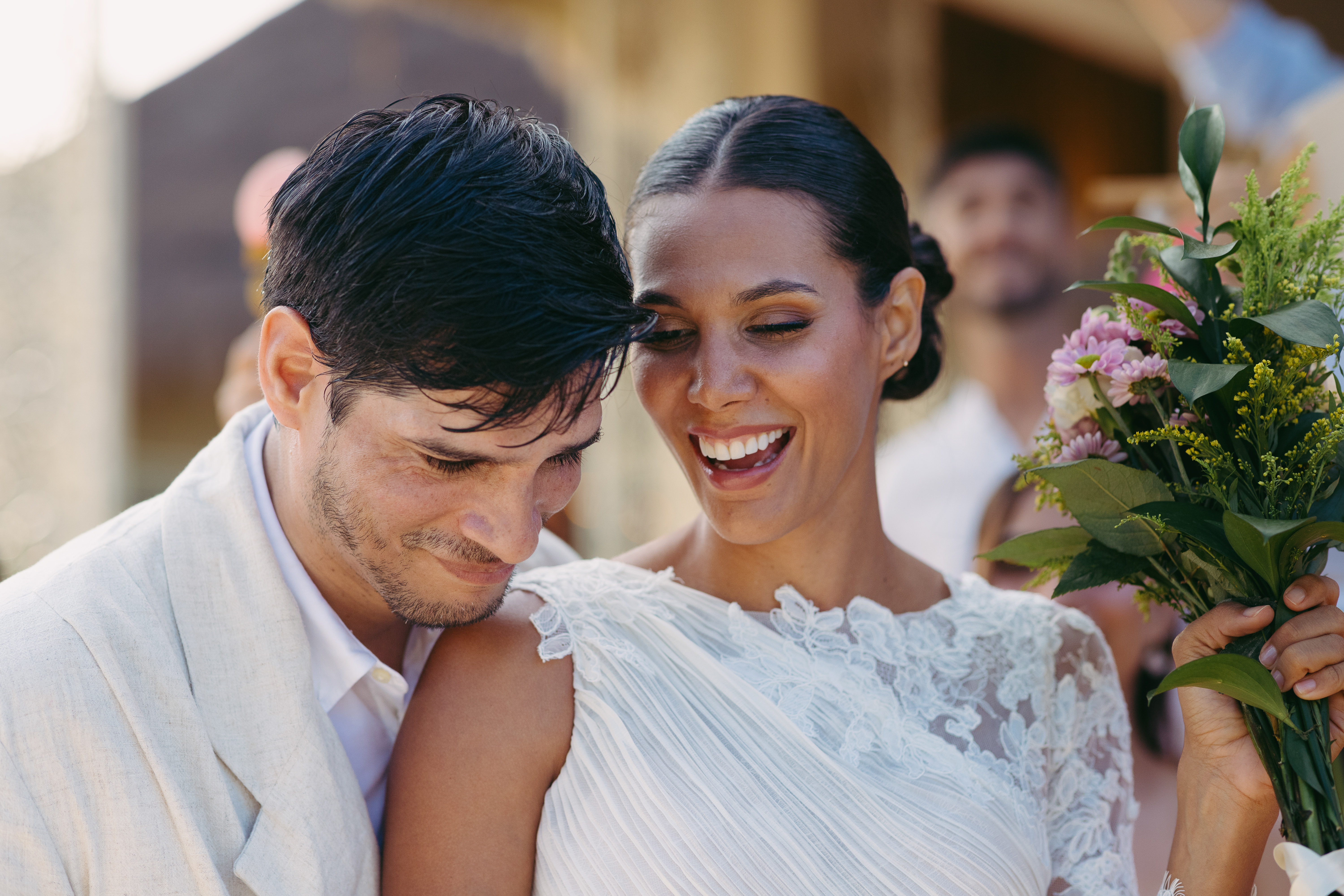 Joyful bride and groom, bride in white lace dress holds flower bouquet.