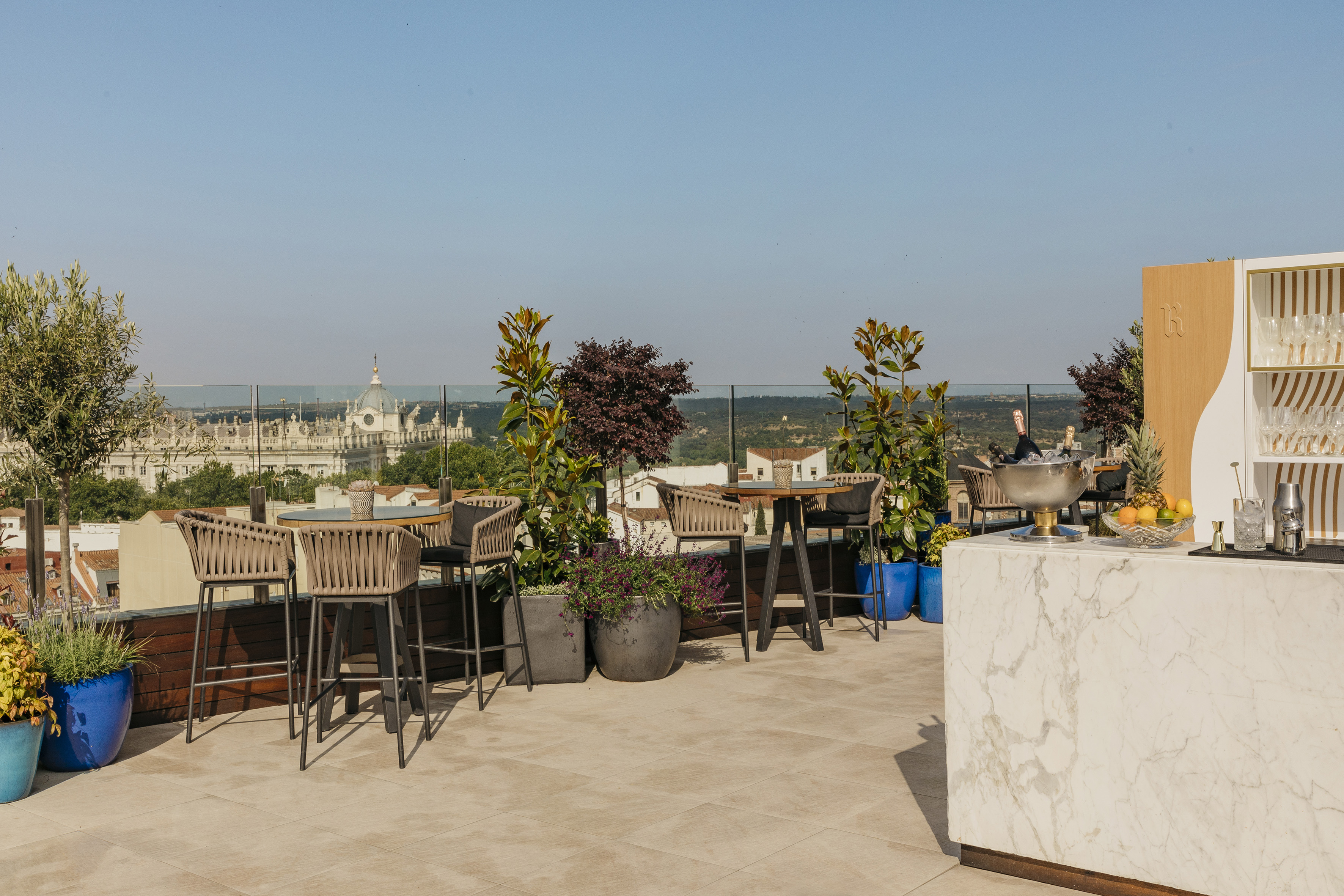 Rooftop terrace bar overlooking Madrid city and Royal Palace with outdoor seating.