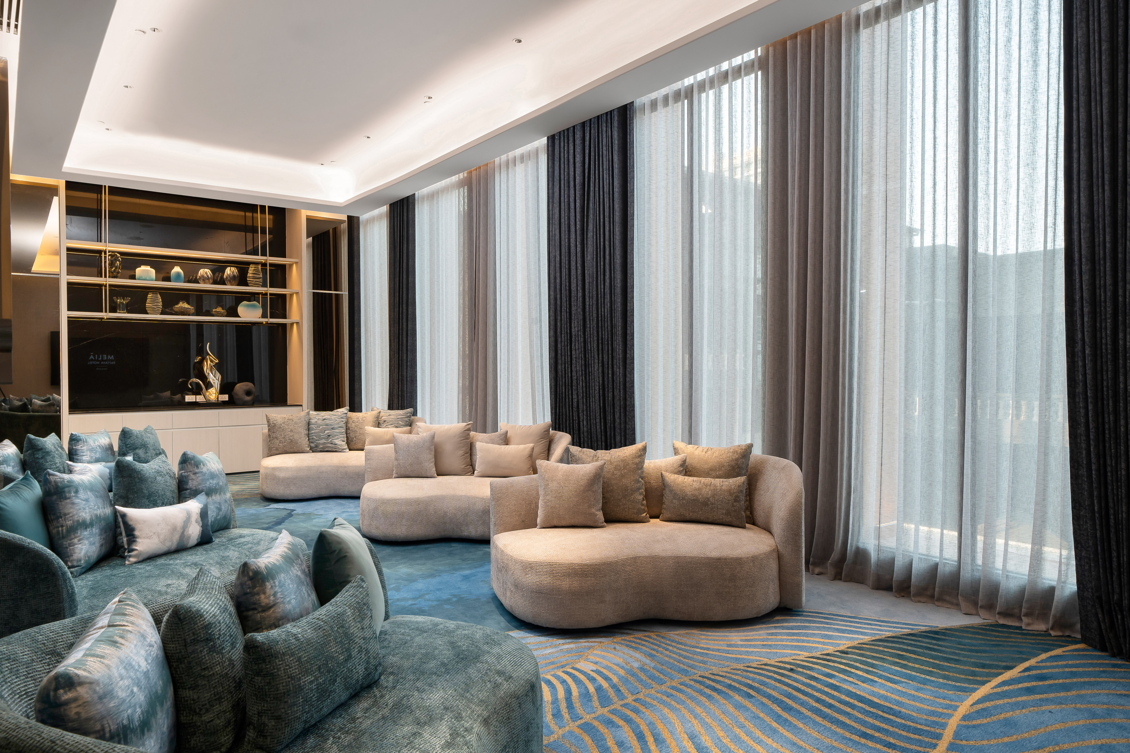 Modern lounge with curved sofas, blue patterned rug, and sheer window curtains.