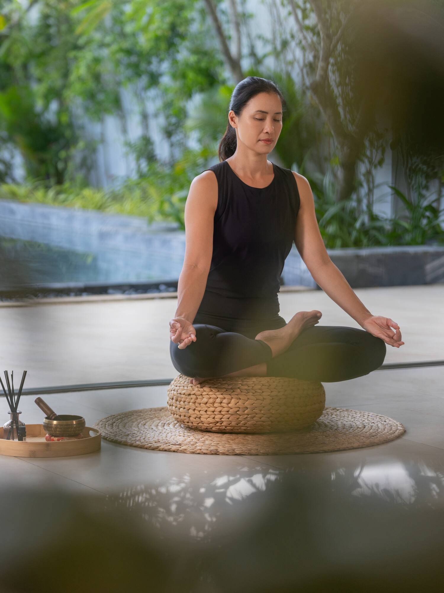 Woman meditating in lotus pose on a cushion in a tranquil garden setting.