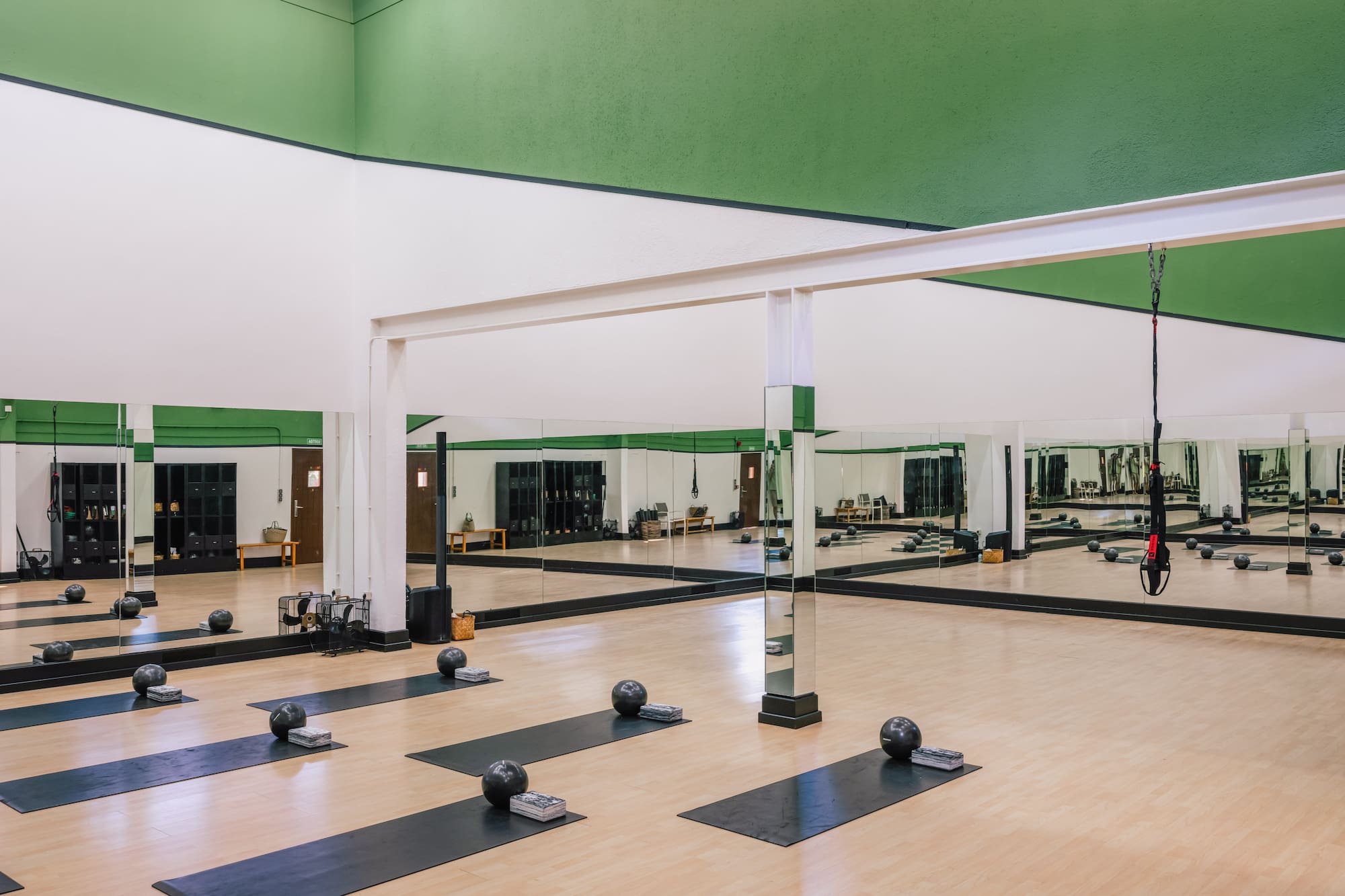 Green and white fitness studio with yoga mats, weighted balls, and mirrored walls.