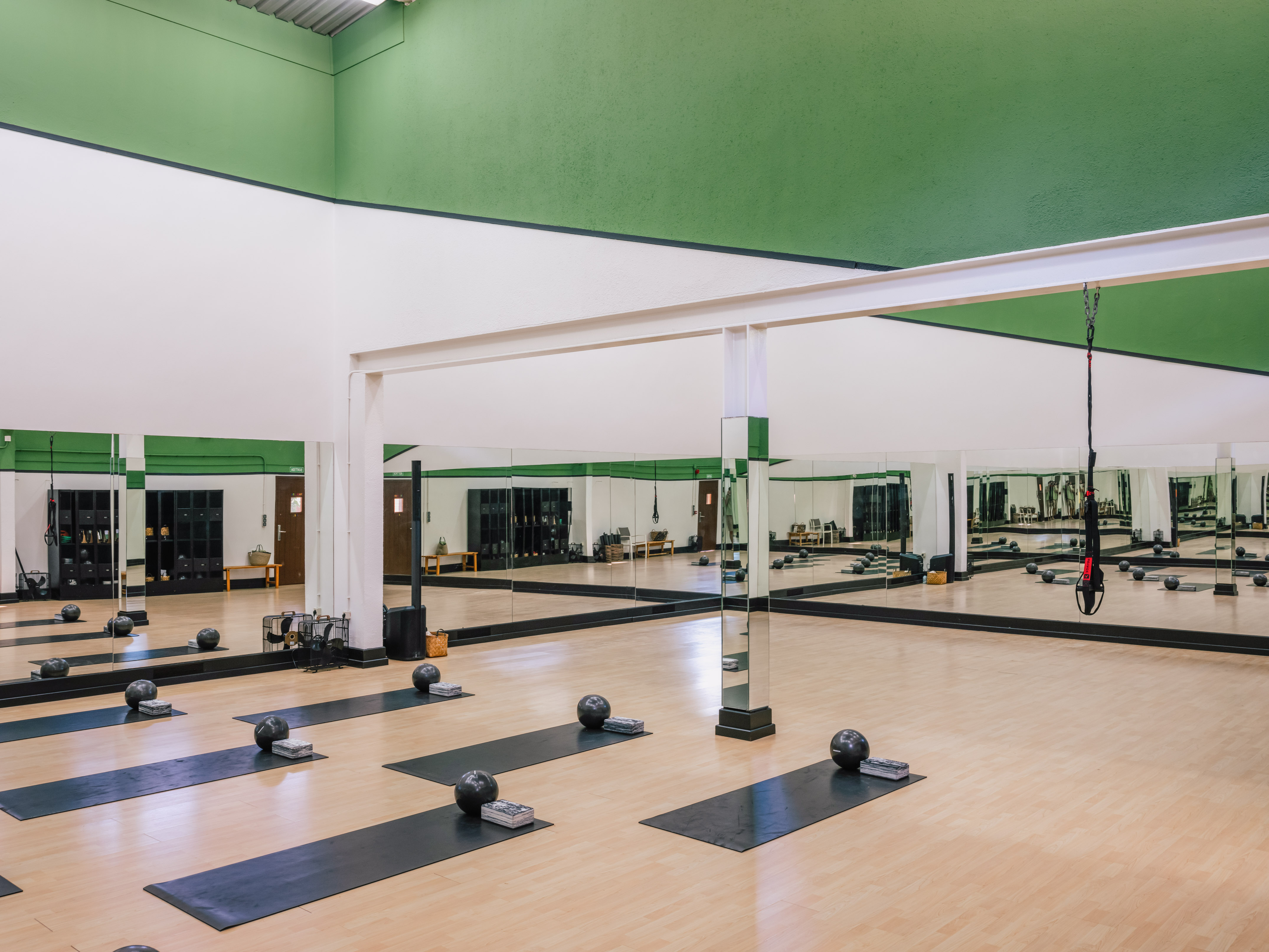 Green and white fitness studio with yoga mats, weighted balls, and mirrored walls.