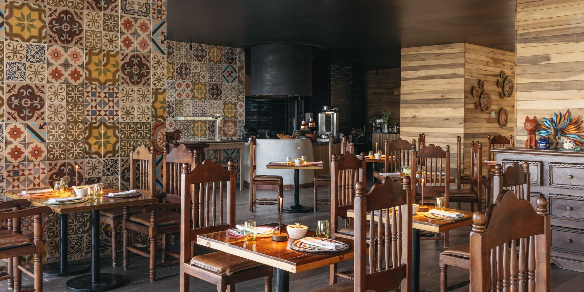Vibrant restaurant interior with patterned tiles, wooden tables, and open kitchen area.