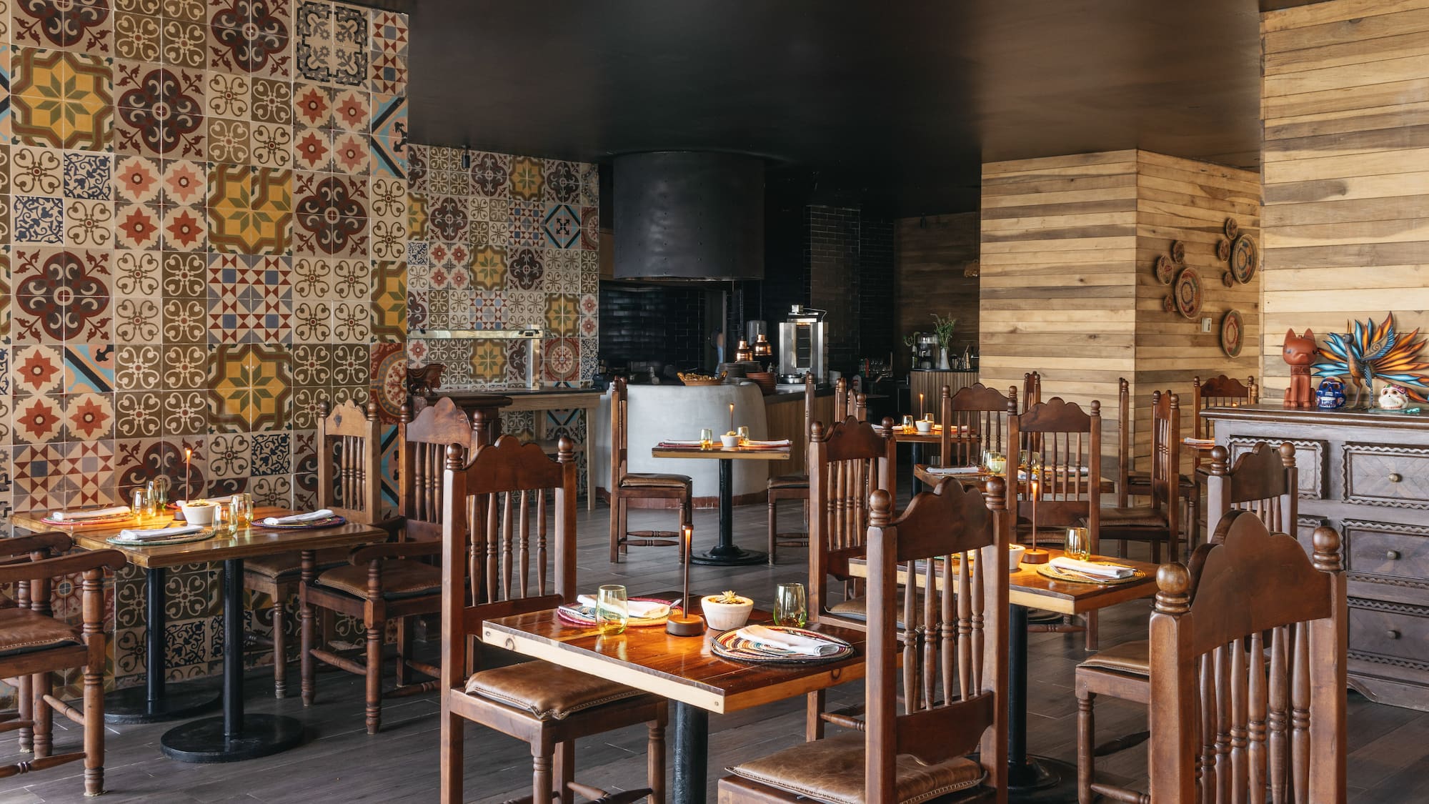 Vibrant restaurant interior with patterned tiles, wooden tables, and open kitchen area.