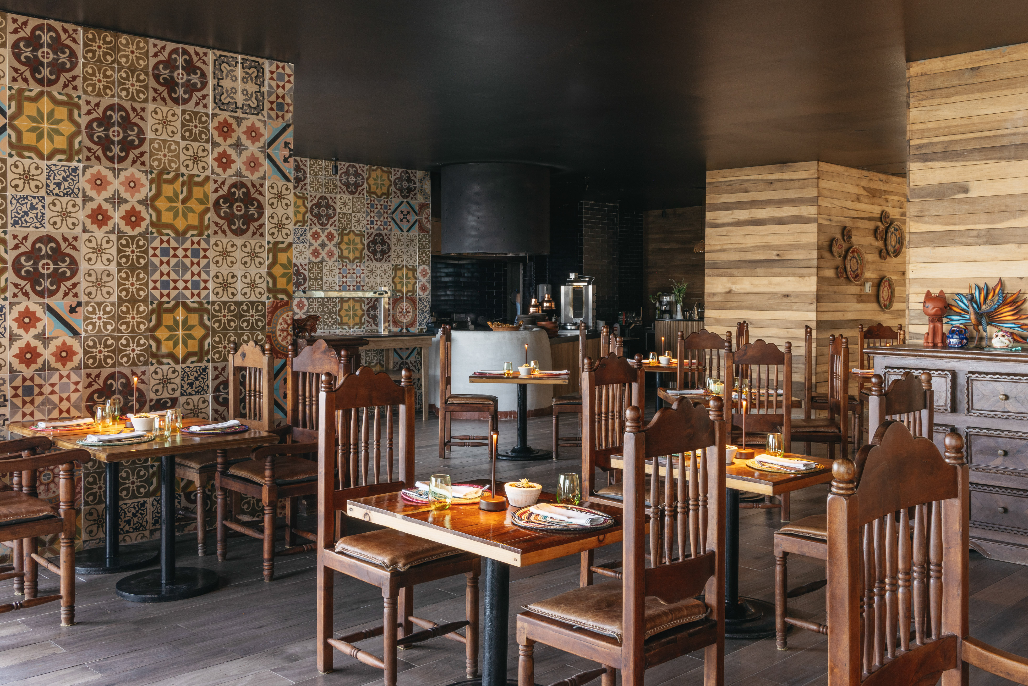 Vibrant restaurant interior with patterned tiles, wooden tables, and open kitchen area.