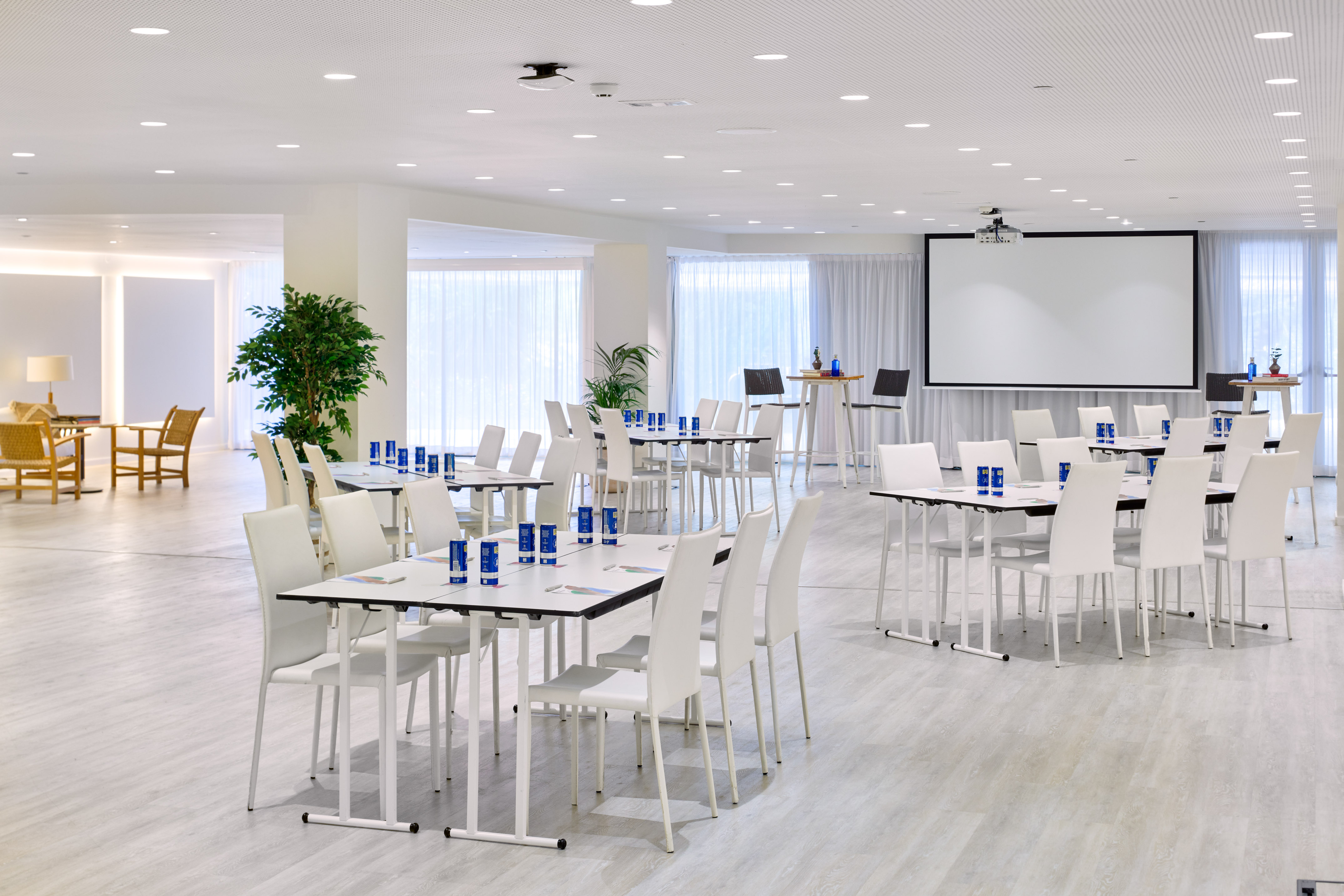Bright modern conference room with white tables, chairs, projector, and plants for events.