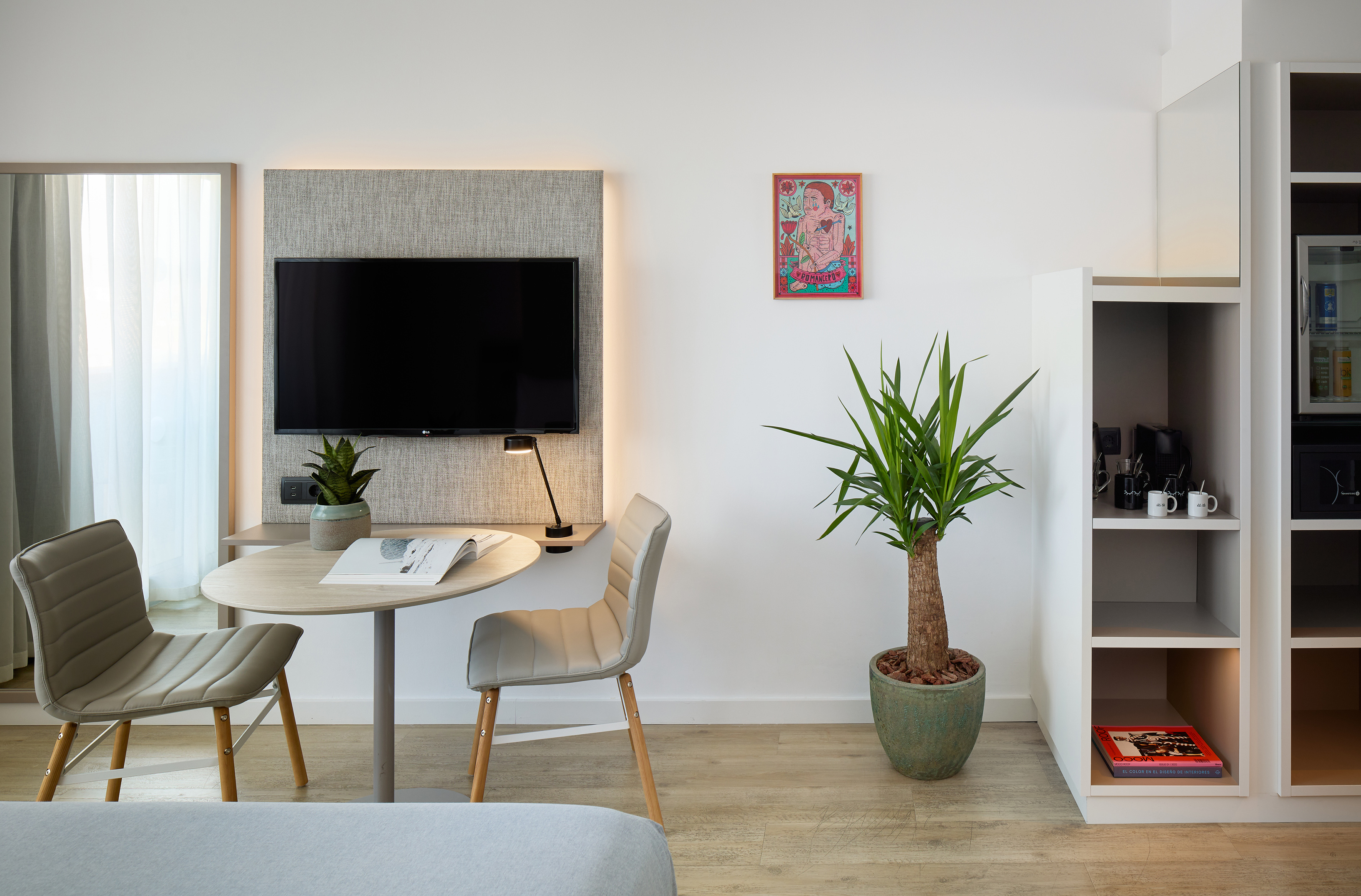 Contemporary hotel room with desk, TV, coffee bar, and green plants.