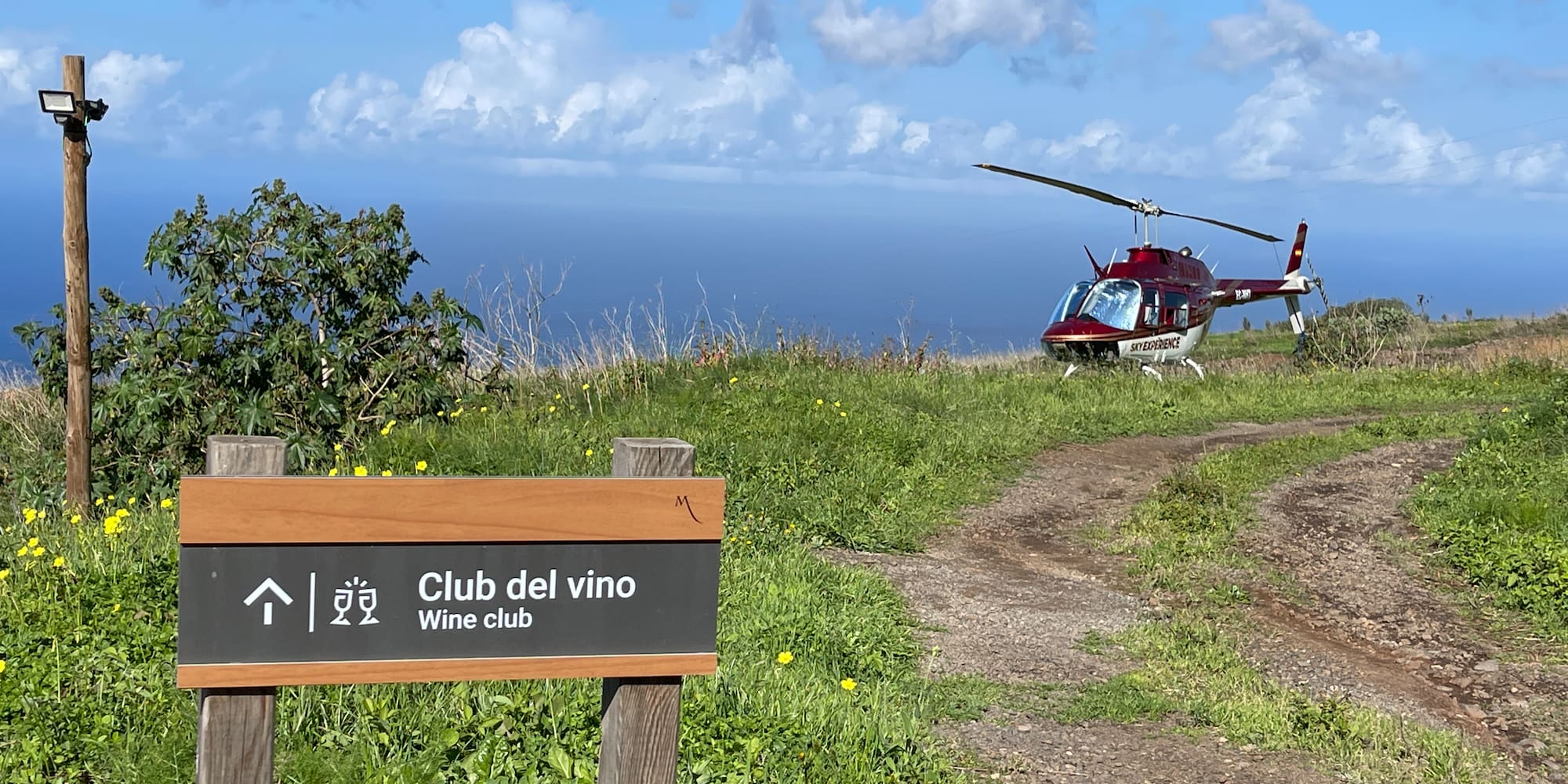 Wine club sign, red Sky Experience helicopter on coastal path with ocean view.