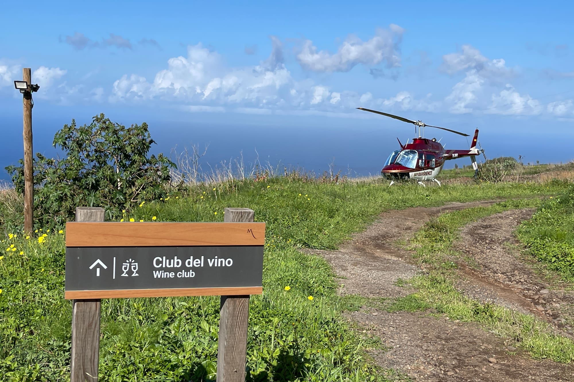 Wine club sign, red Sky Experience helicopter on coastal path with ocean view.