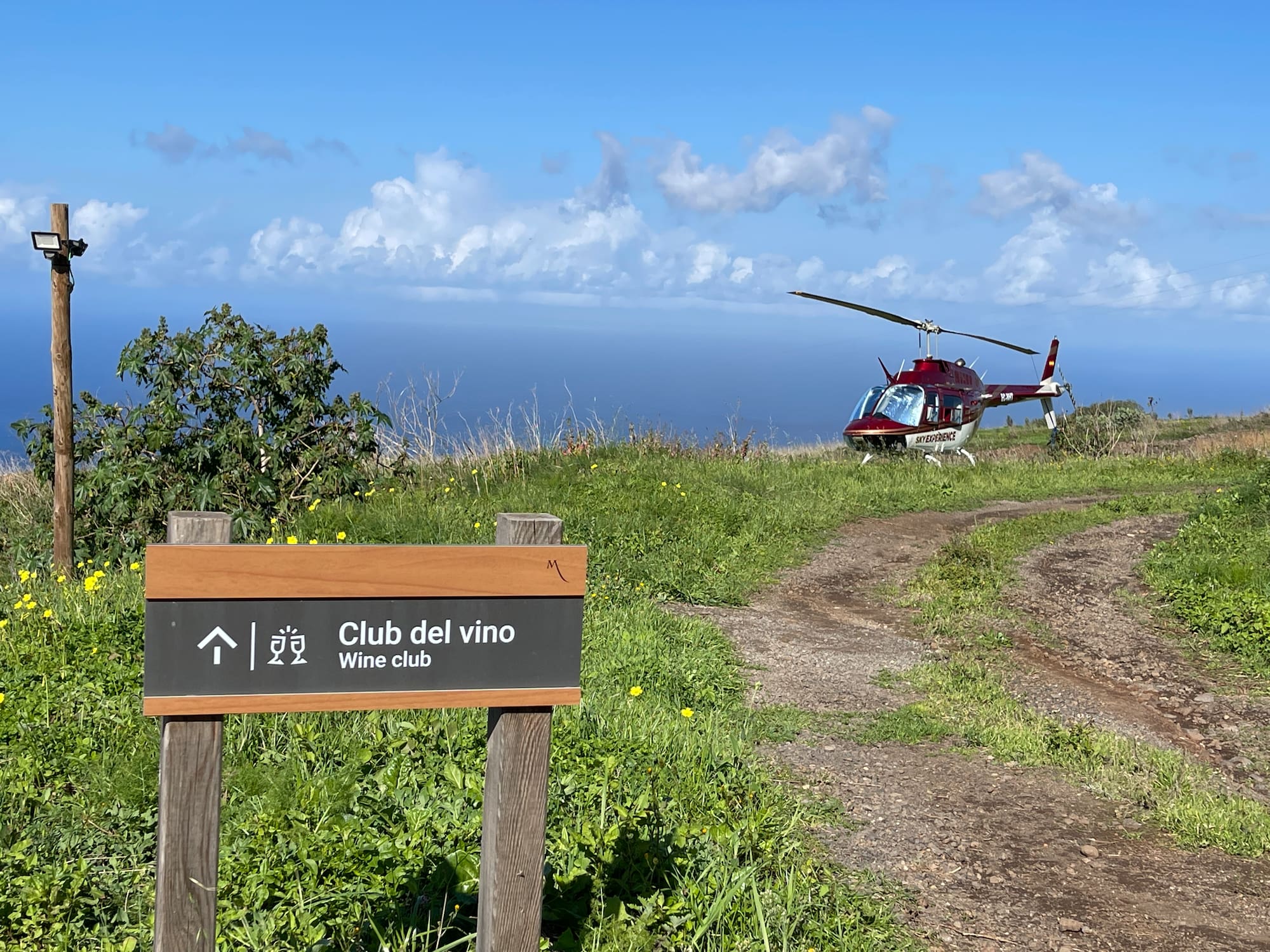Wine club sign, red Sky Experience helicopter on coastal path with ocean view.