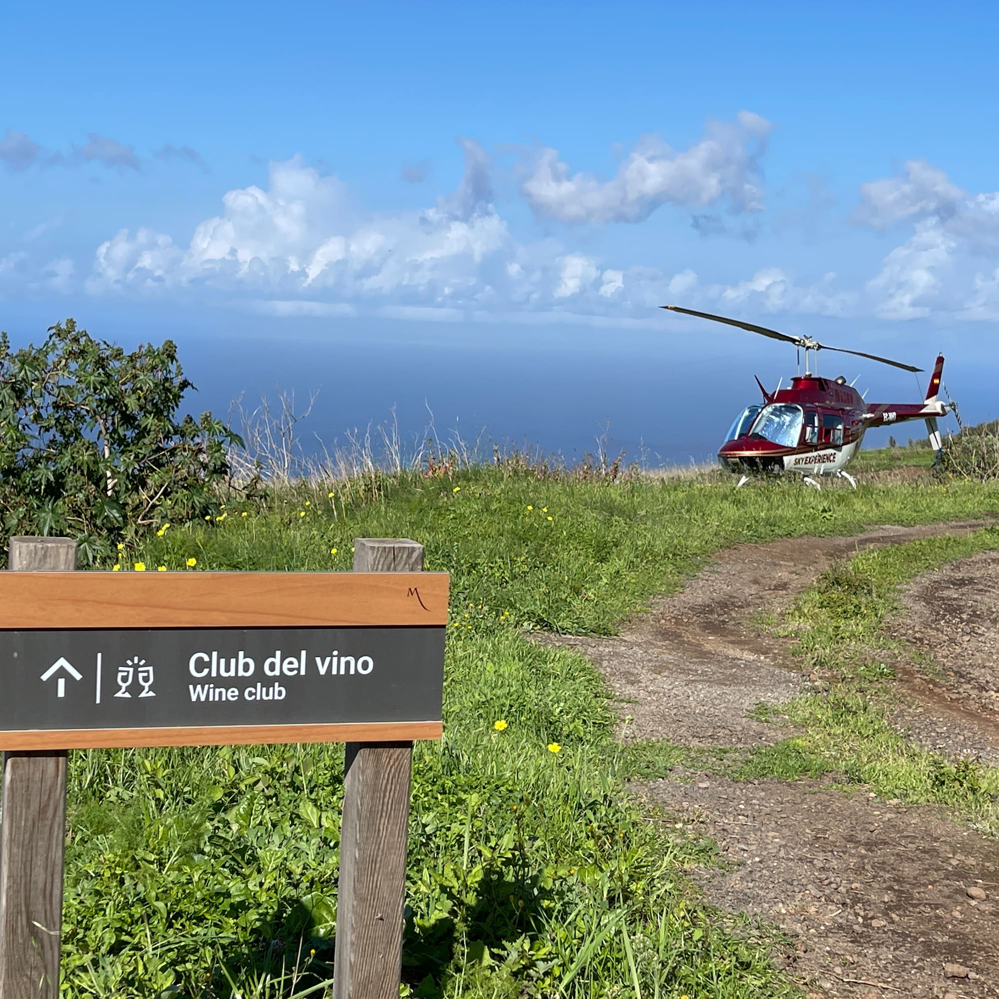Wine club sign, red Sky Experience helicopter on coastal path with ocean view.