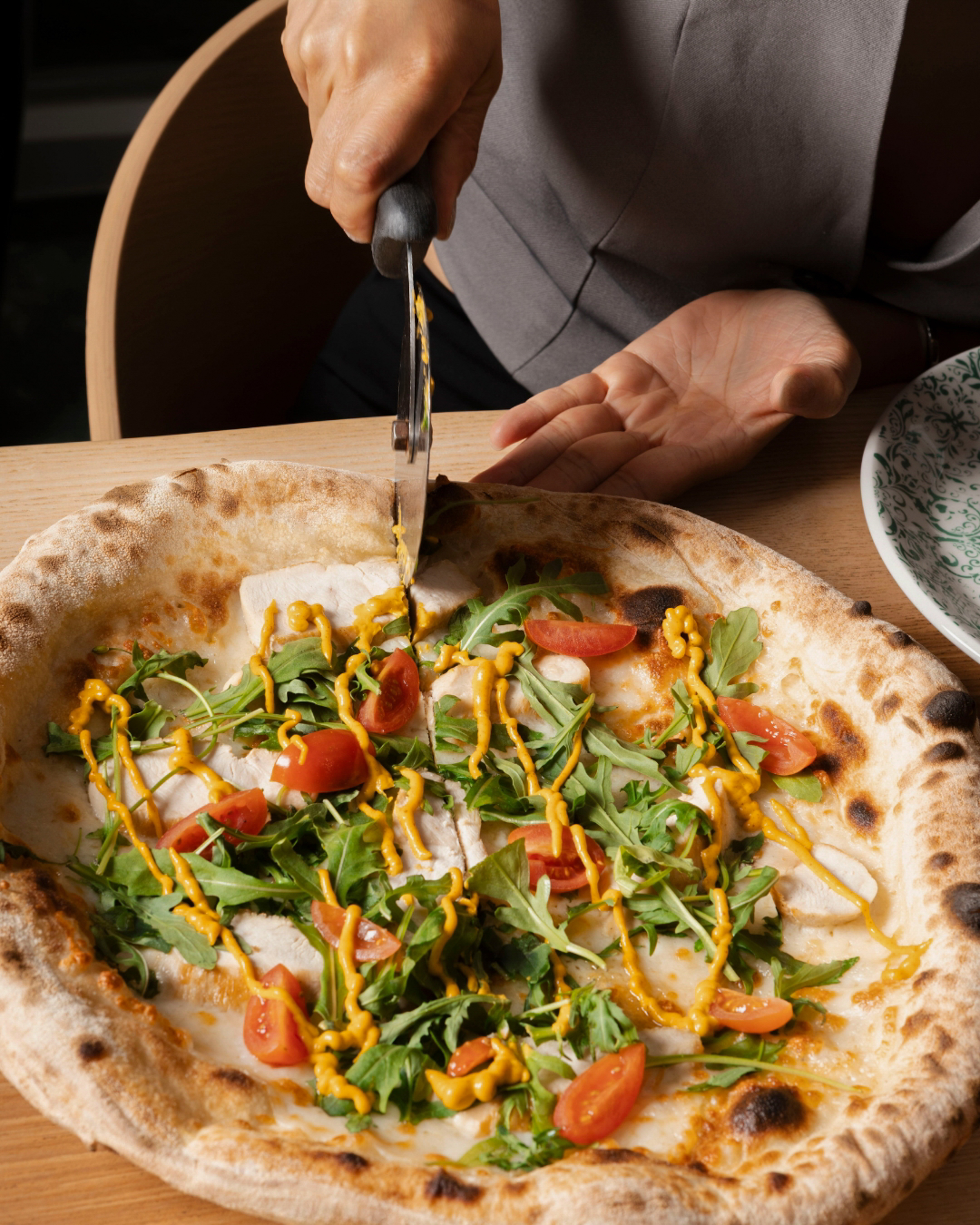 Neapolitan chicken pizza with arugula, tomatoes, mustard being cut.
