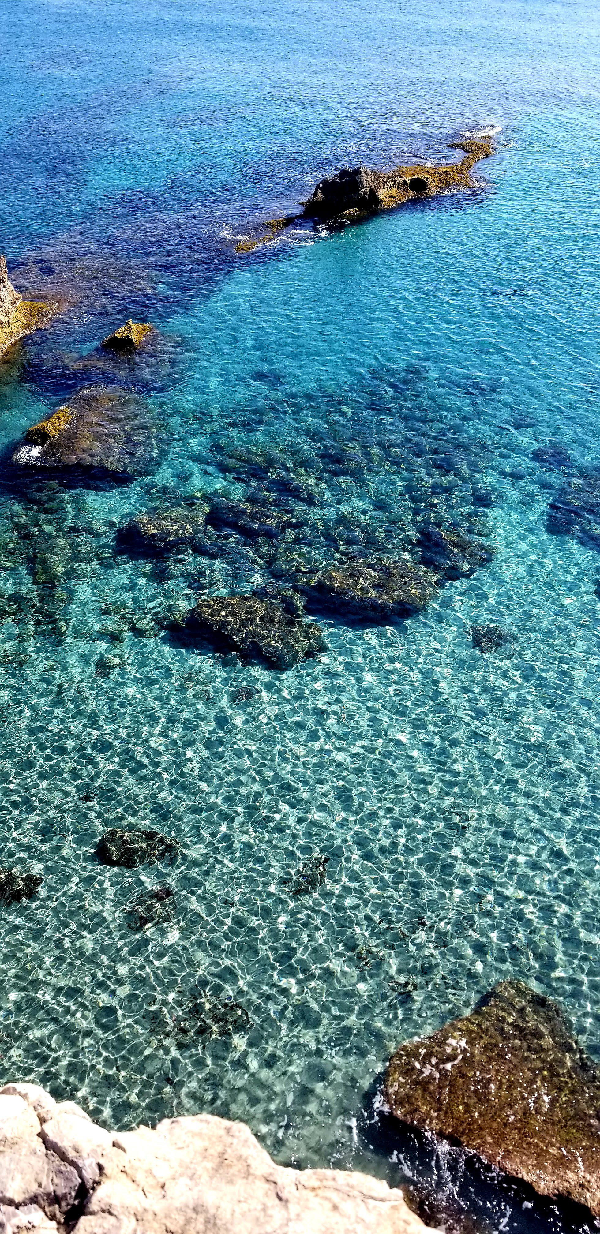 Clear turquoise sea with visible rocky seabed and sunlit water patterns.