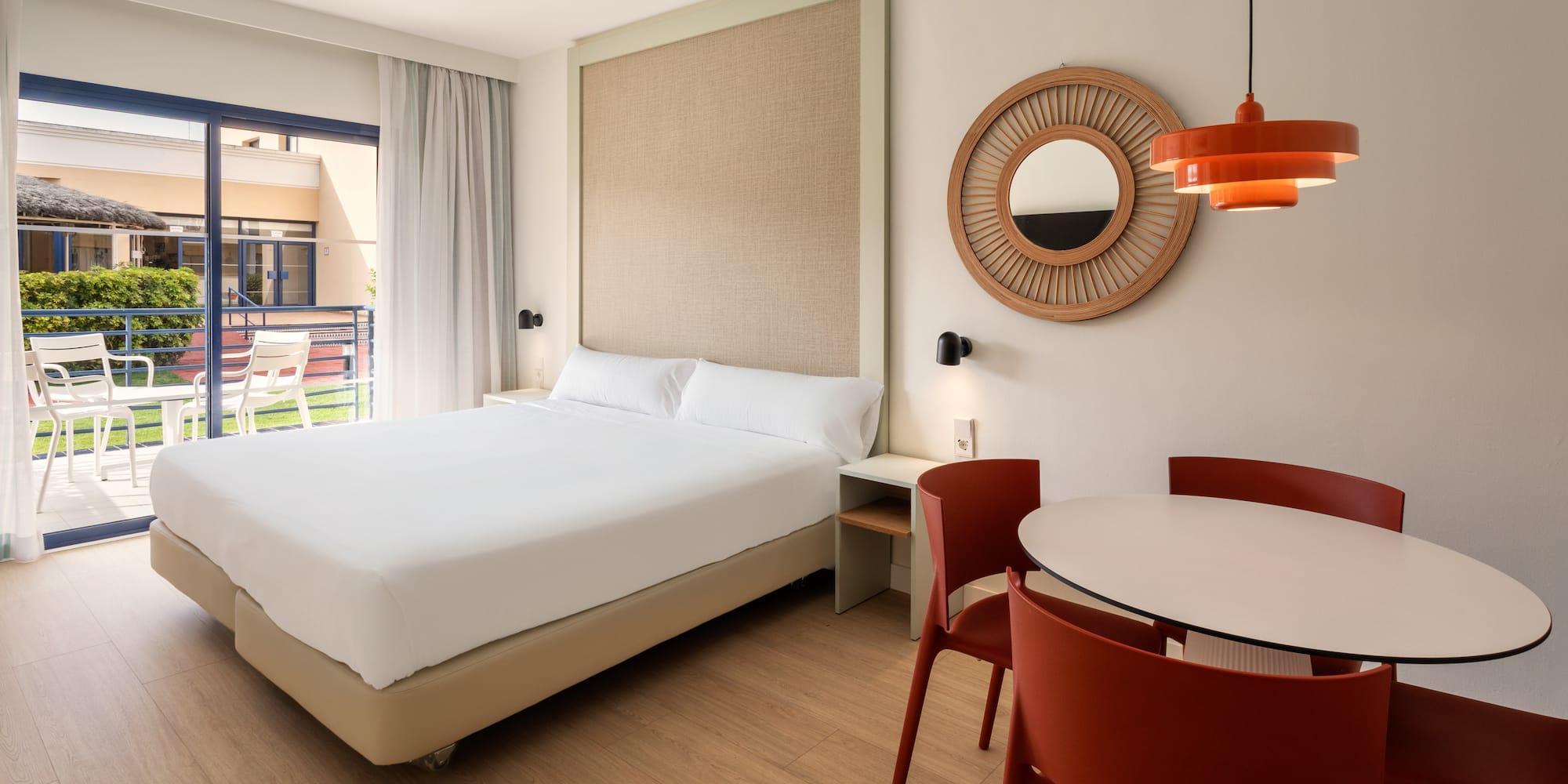 Bright hotel suite with double bed, dining table, and private balcony.