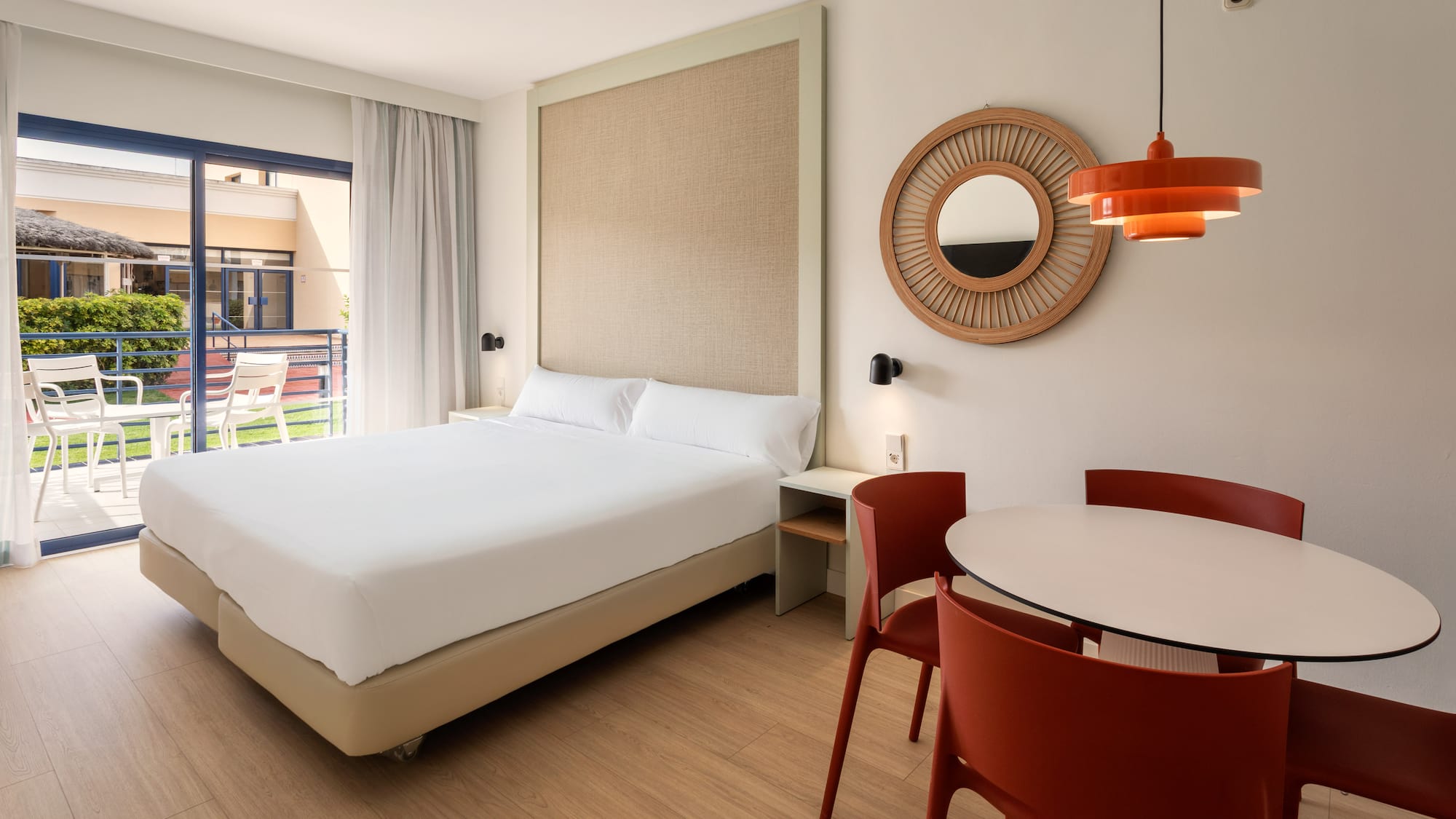 Hotel suite with bed, red dining chairs, and a private balcony.