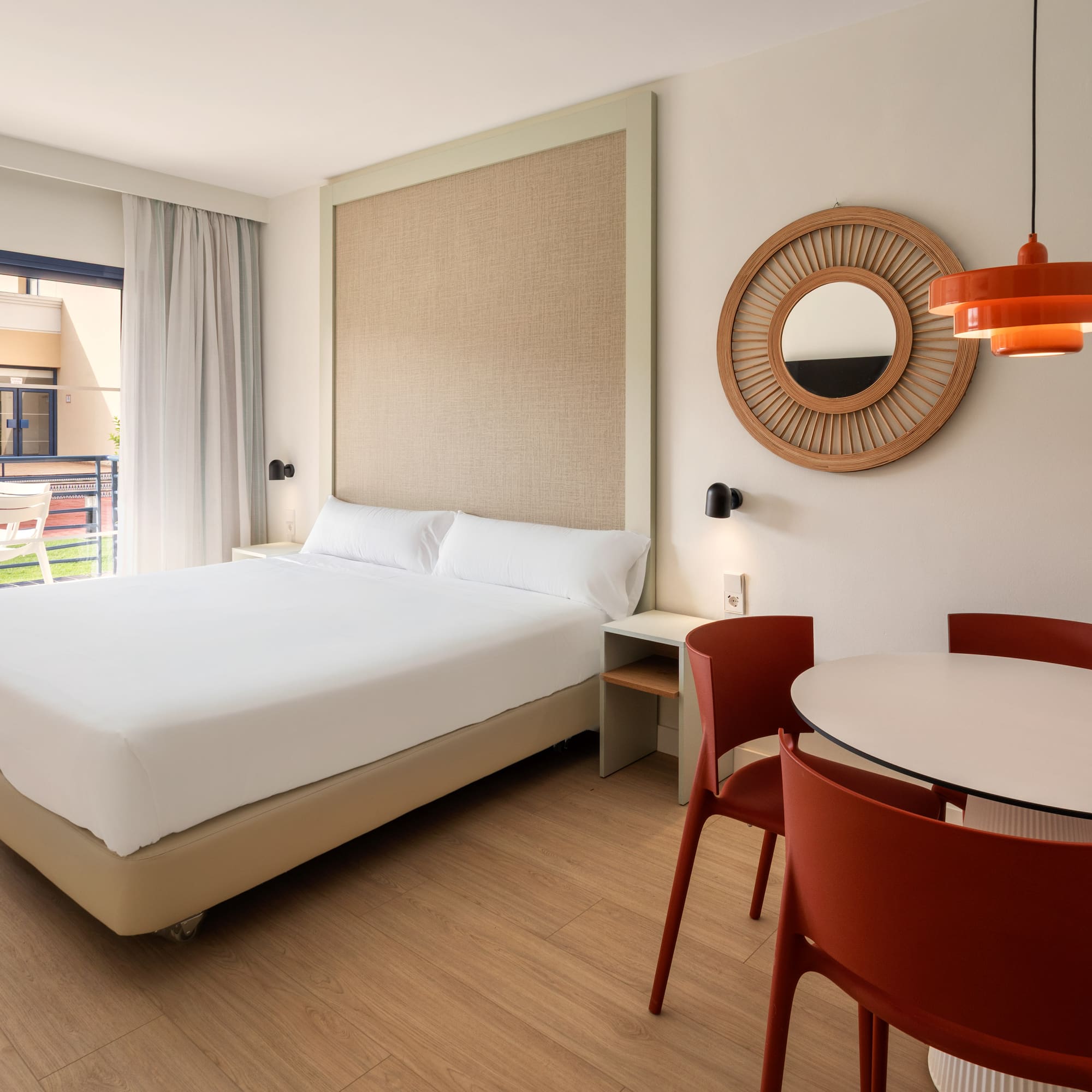 Bright hotel suite with double bed, dining table, and private balcony.