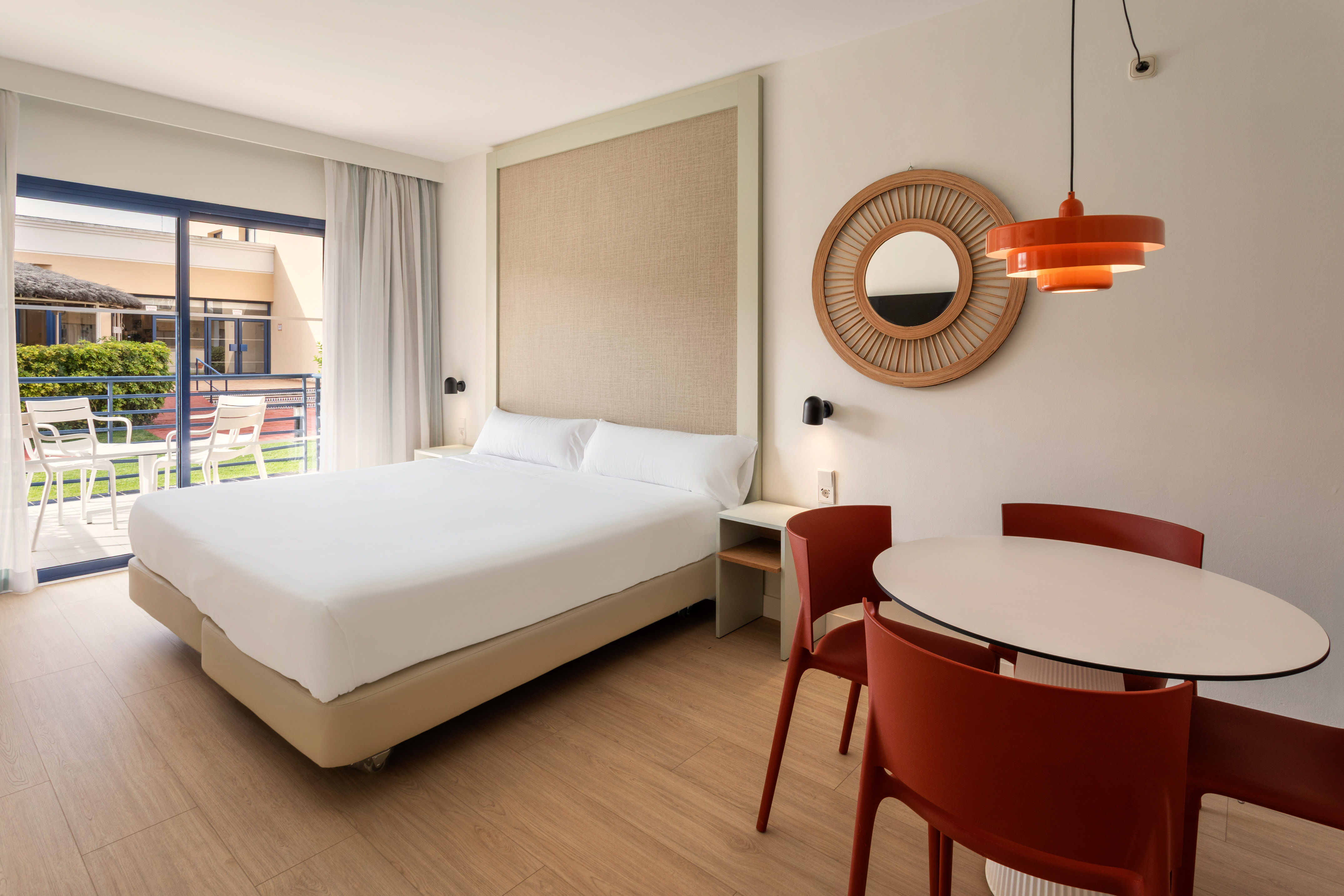 Hotel suite with bed, red dining chairs, and a private balcony.