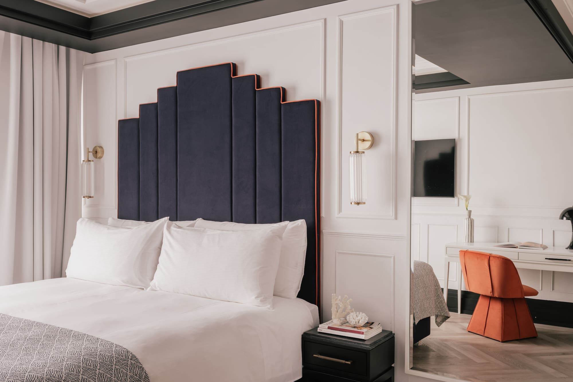 Modern bedroom with navy Art Deco headboard and orange chair.